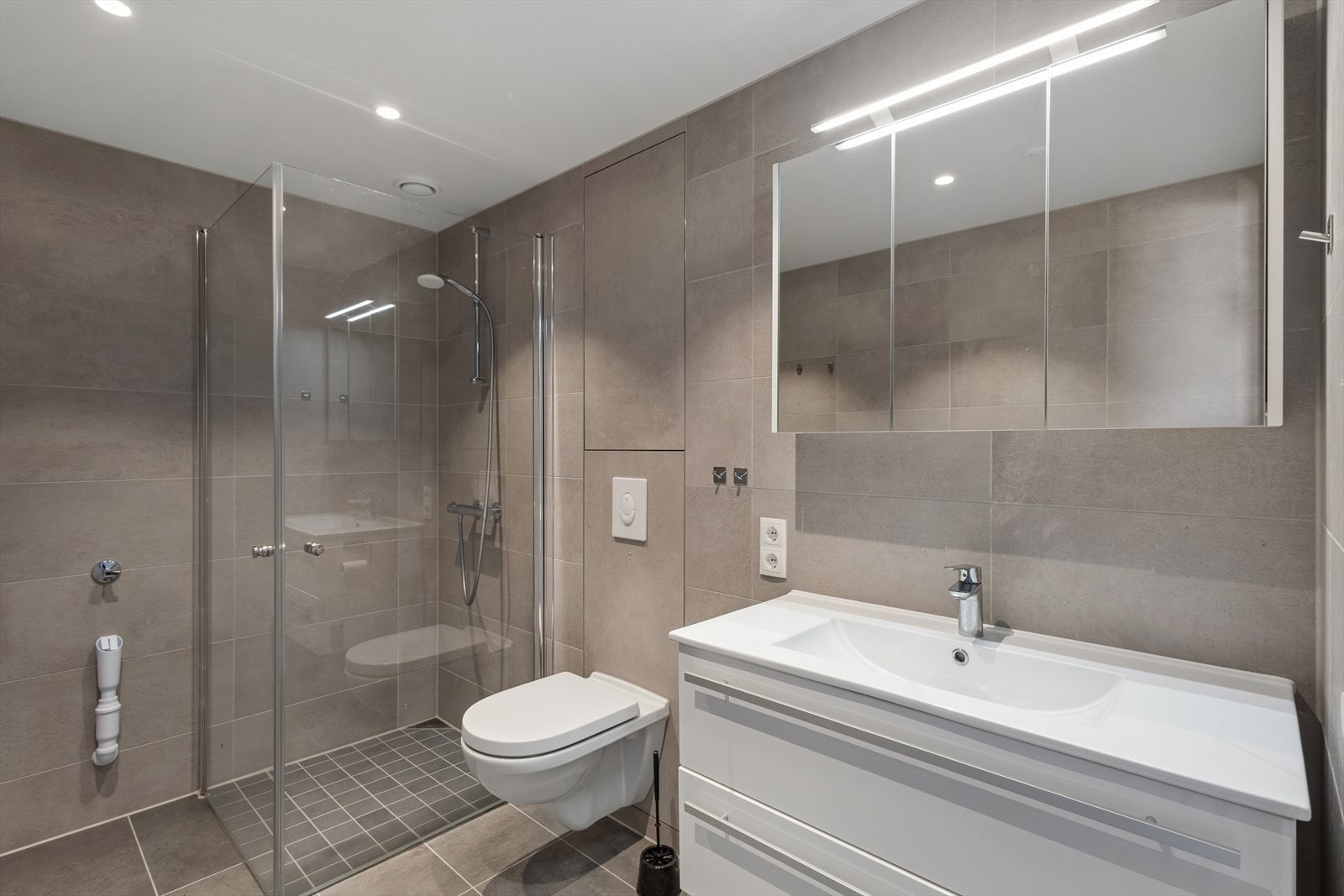 Badet fremstår lekkert og praktisk, med opplegg for vaskemaskin og vannbåren gulvvarme. Galleribilde