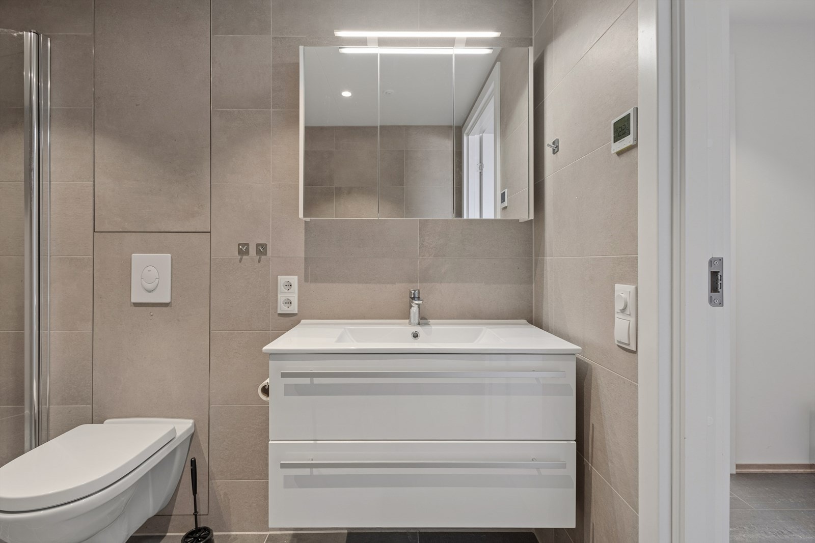 Badet har en moderne og funksjonell innredning med servantskap, speil med integrert belysning og vegghengt toalett fra 2025. Galleribilde