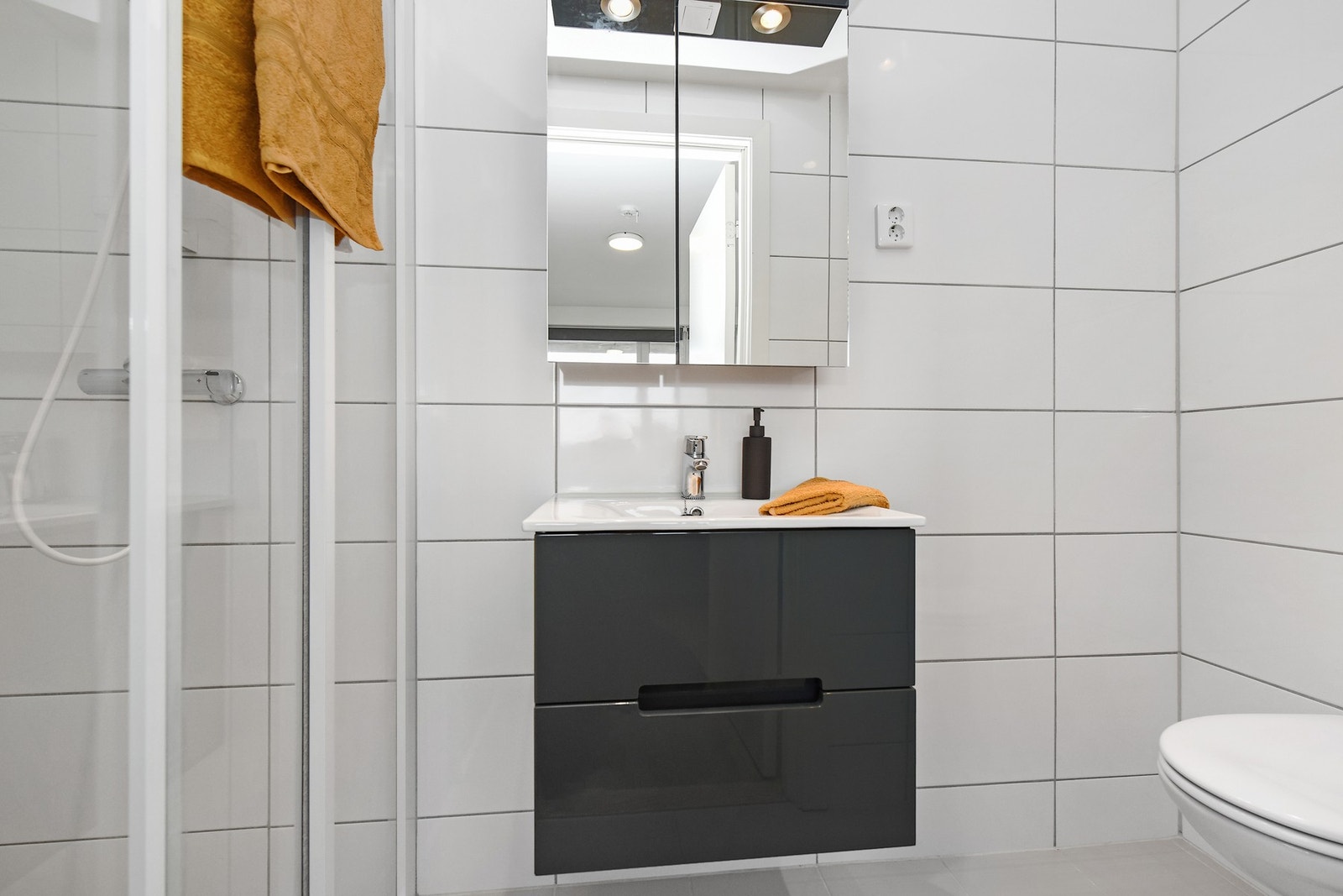 Badet er flislagt og er innredet med dusjnisje, edfelt servant og veggfestet toalett. Videre er det varmekabler i gulv og avtrekk via balansert ventilasjon. Galleribilde