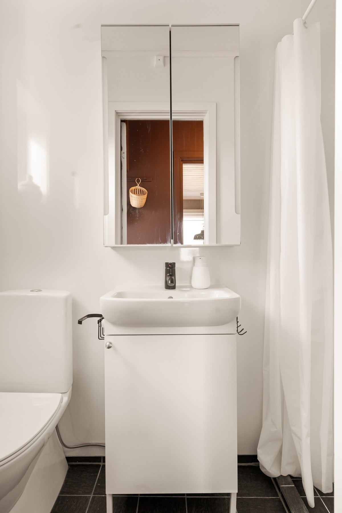 Badet har fliser på gulvet, skapinnredning med servant, speilskap, toalett og dusjhjørne. Galleribilde