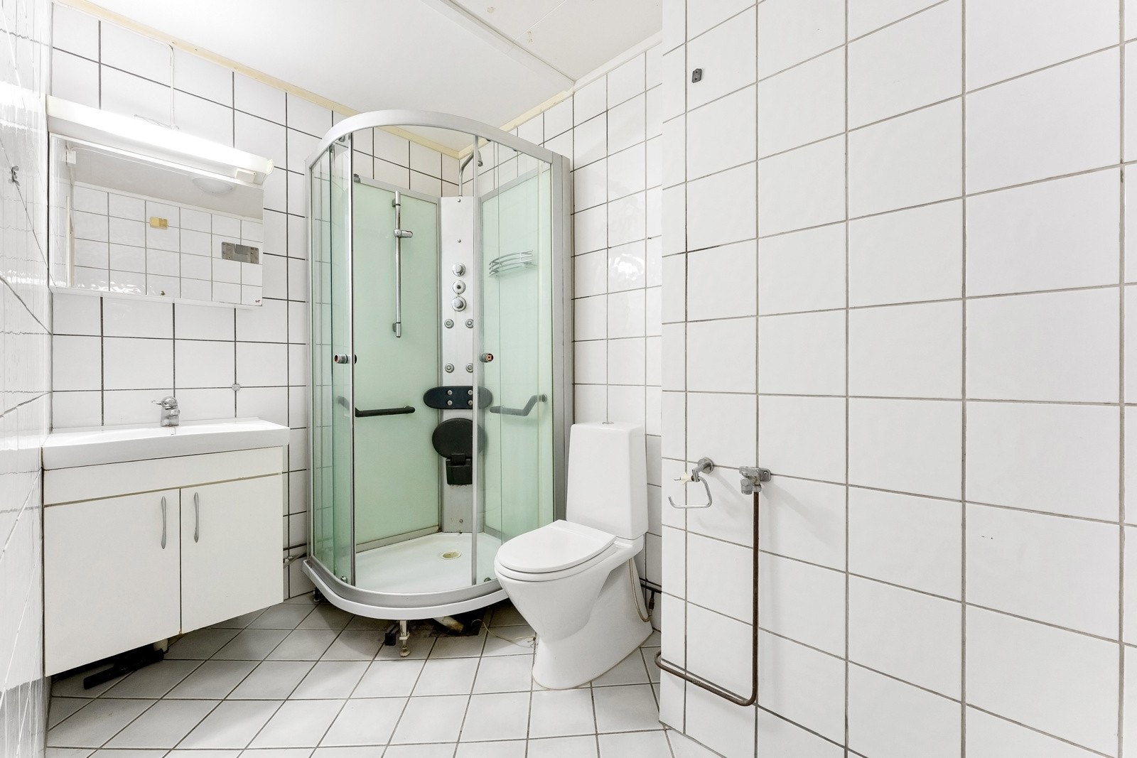 Flislagt baderom med varmekabler, klosett, dusjkabinett, servant og overskap med belysning Galleribilde