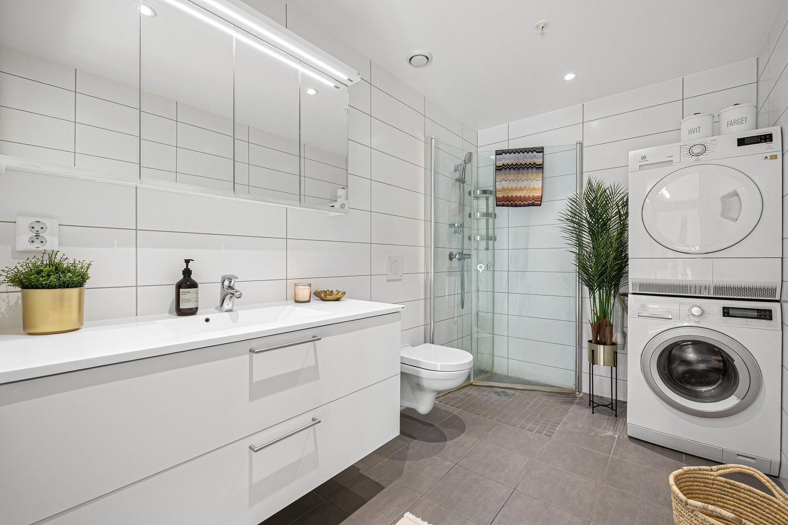 Badet er utstyrt med vegghengt WC, stor servant, dusjhjørne med innfellbare dører og opplegg for vaskemaskin. Galleribilde