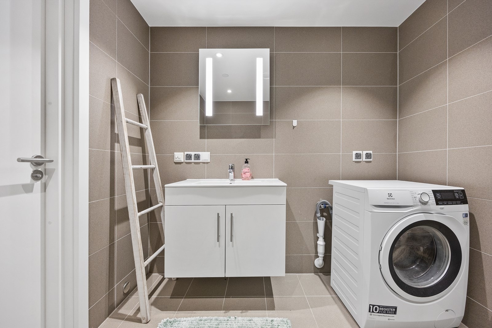 Innredningen består av et hvit servantskap, speil med belysning og opplegg for vaskemaskin. Galleribilde