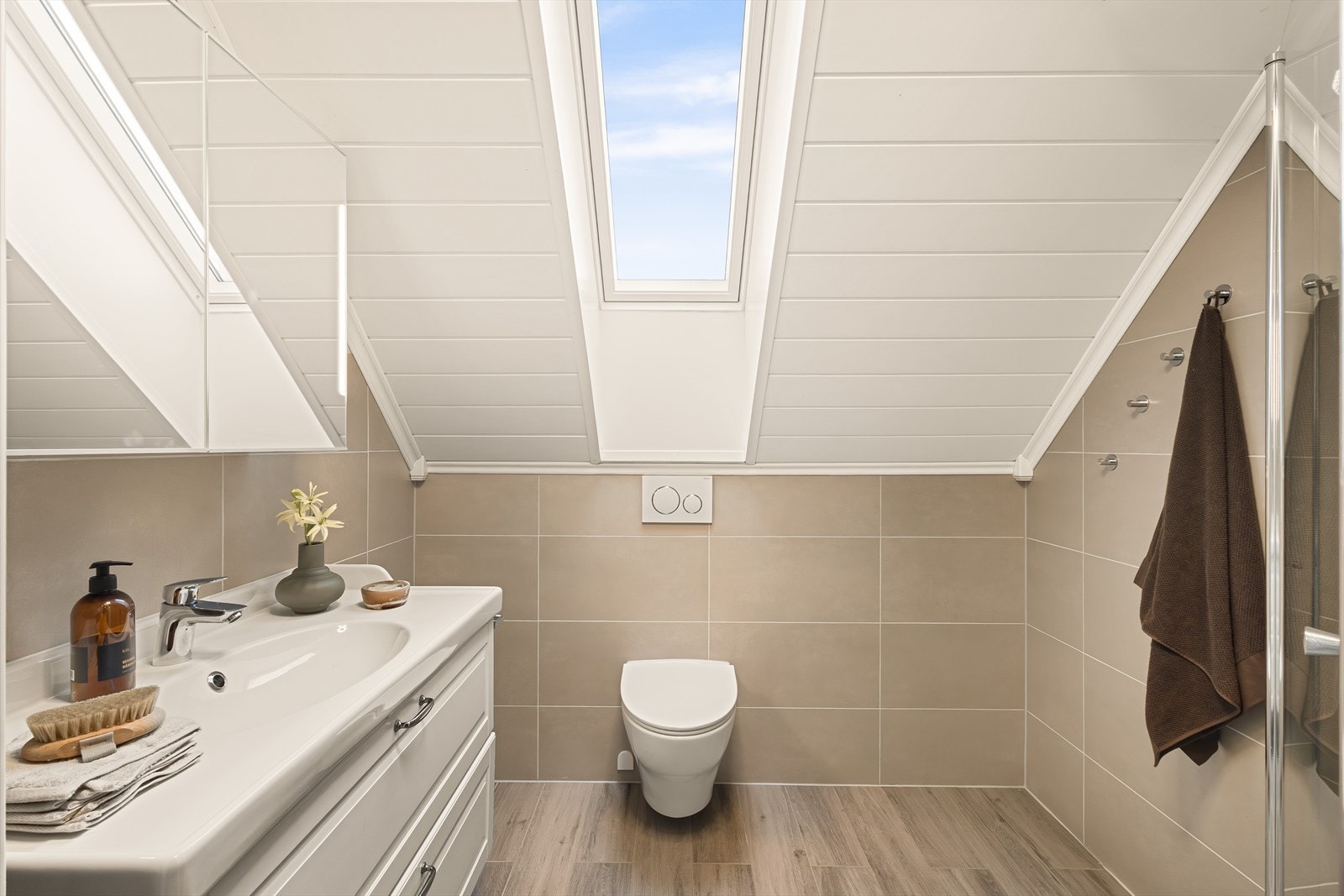 Badet inneholder dusjhjørne, servant med underskuffer, overskap med speil og vegghengt toalett. Galleribilde