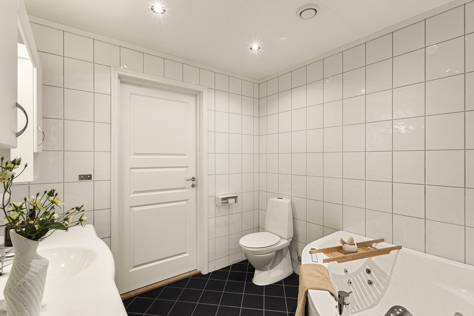 Badet er innredet med baderomsinnredning med hvite, glatte fronter og heldekkende servant, overskap og speil, toalett, hjørnebadekar med massasjedyser samt dusjhjørne med to glassdører. Galleribilde