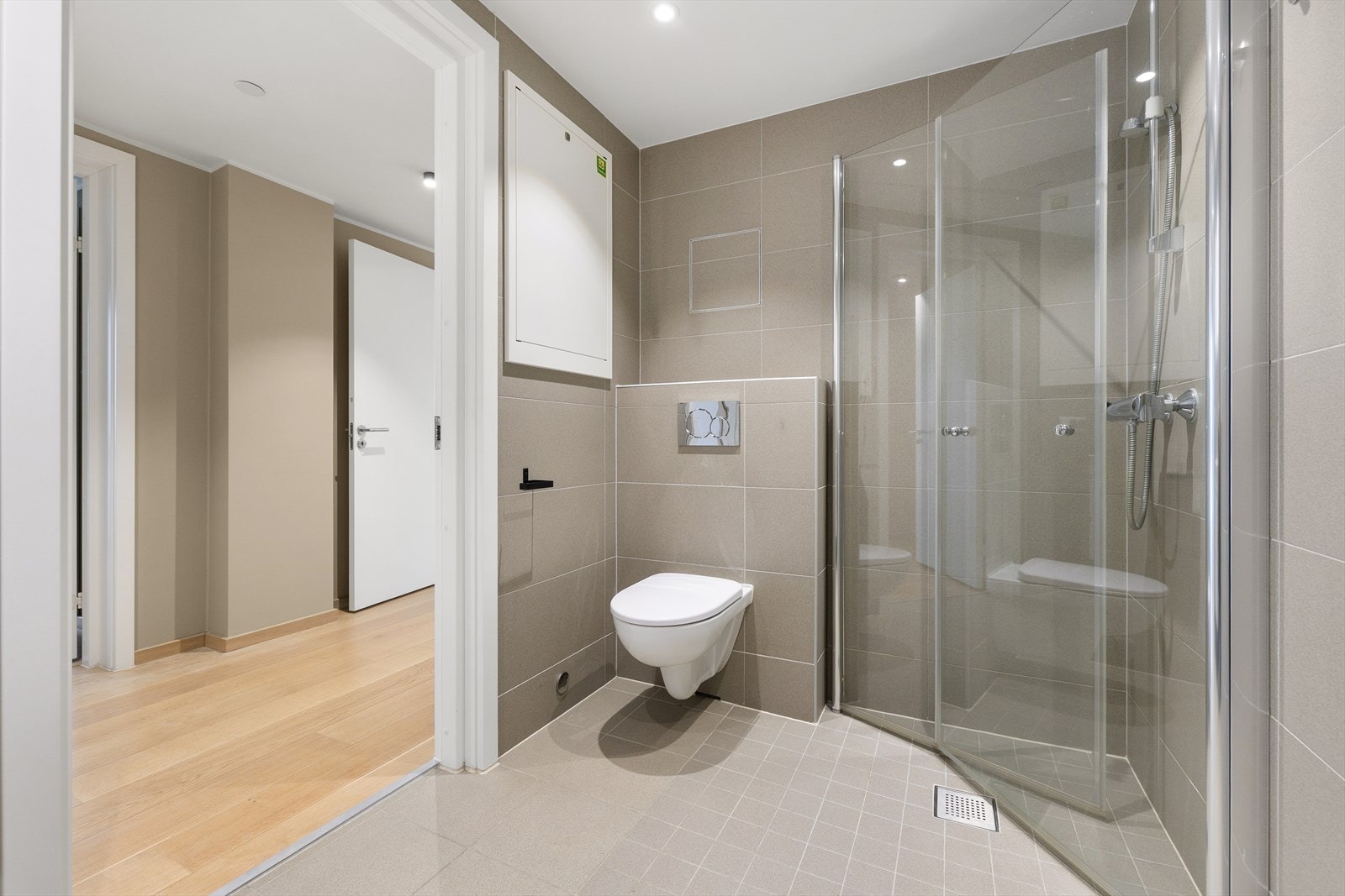 Badet er innredet med vegghengt toalett, dusjhjørne med innfellbare glassvegger og servant i baderomsinnredning. Galleribilde