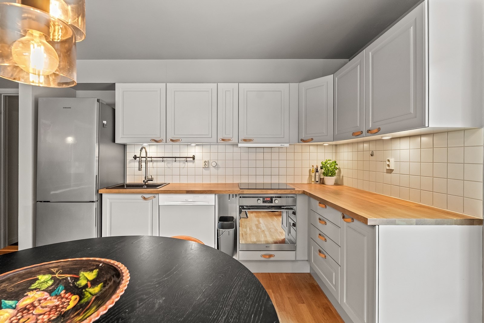 Kjøkkenet er utstyrt med oppvaskkum, ventilator, fliser over benk og belysning under overskap. Integrerte hvitevarer inkluderer oppvaskmaskin, stekeovn og induksjonstopp. Galleribilde