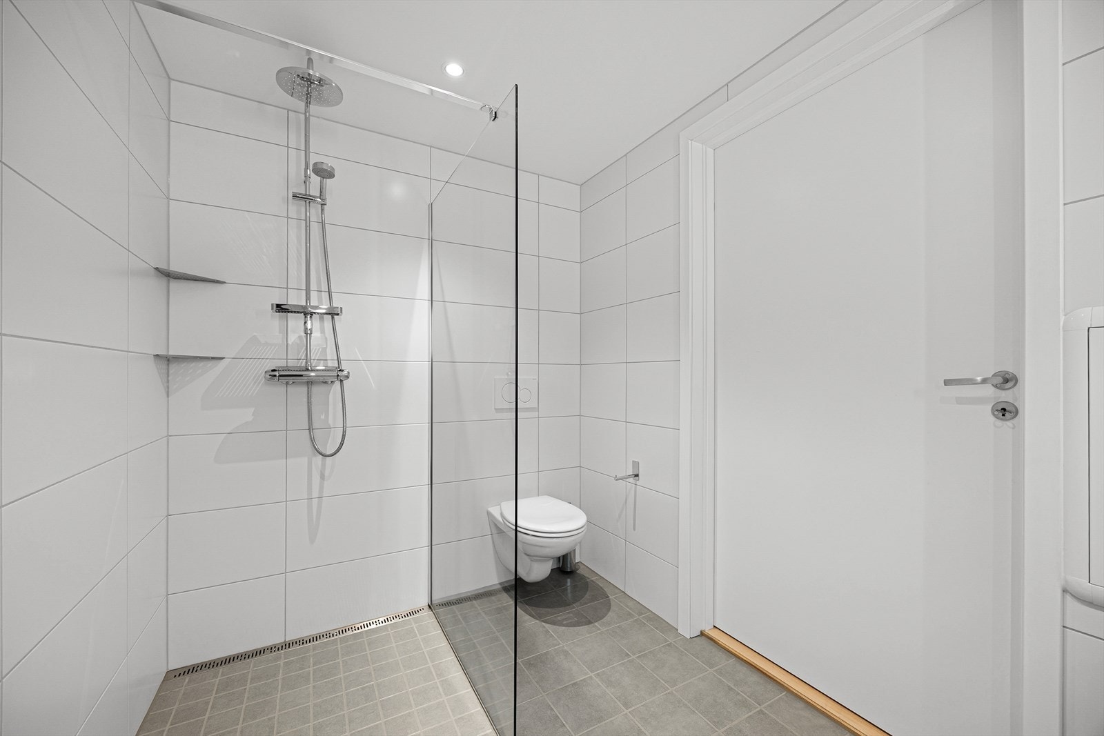 Badet er innredet med veggmontert toalett, dusjnisje med glassvegg og servantinnredning. Galleribilde