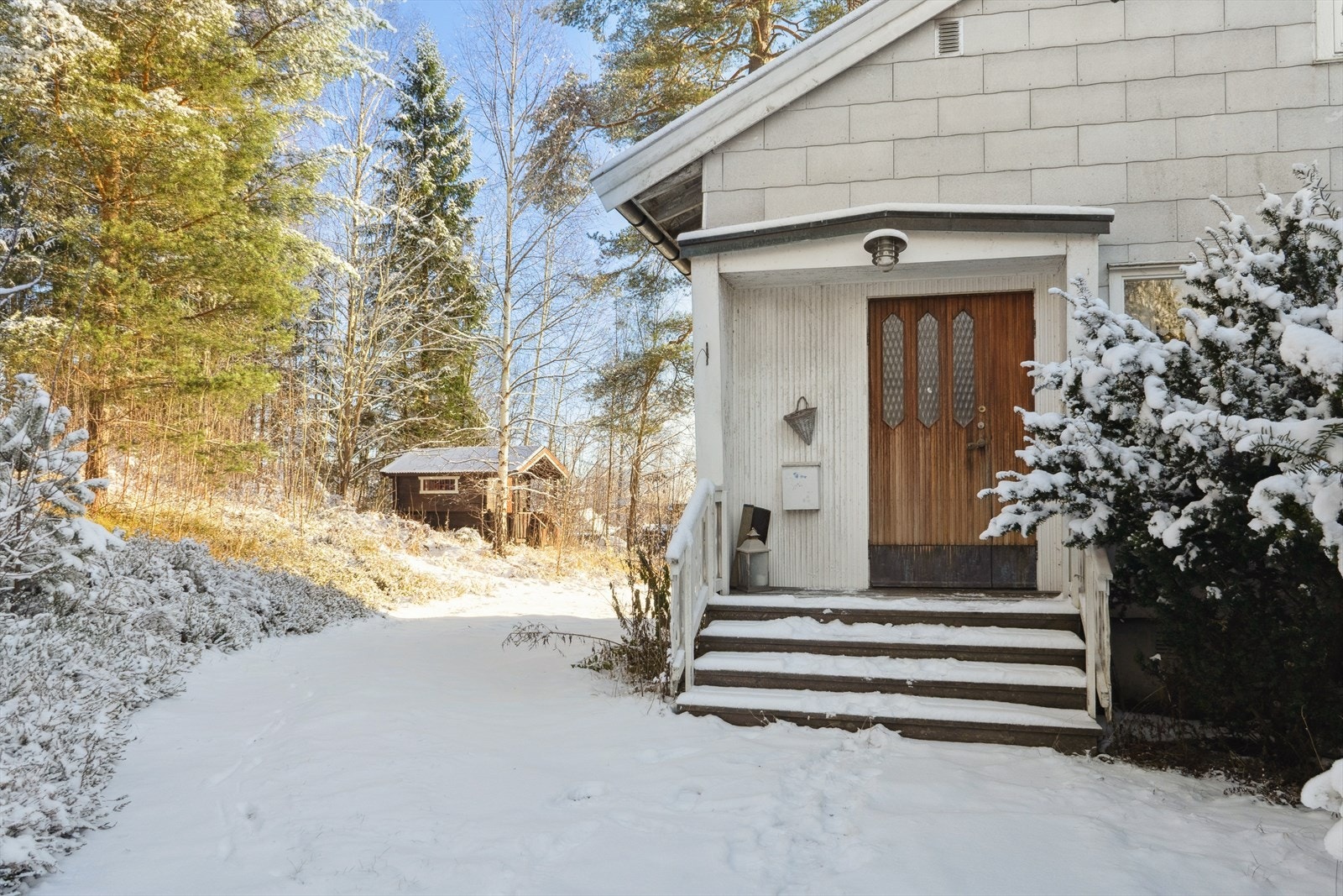 Det delvis takoverbygde inngangspartiet fra 1982 ønsker velkommen. I bakgrunnen skimtes det frittstående stabburet. Galleribilde