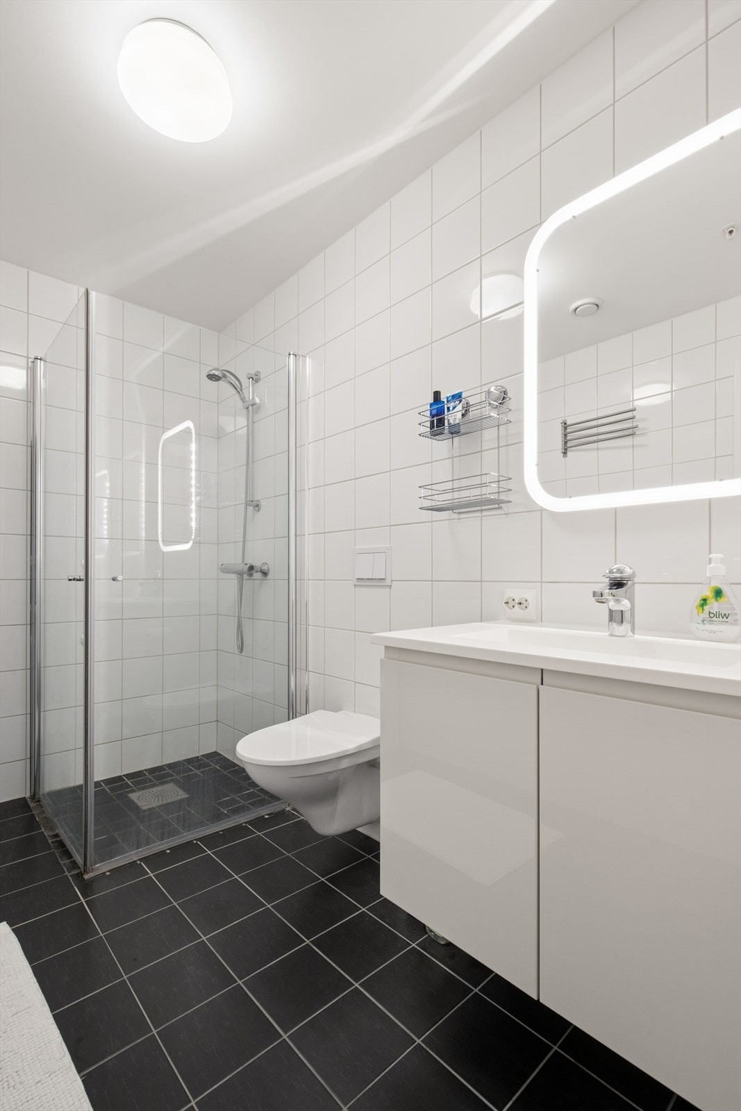 Badet er flislagt og utstyrt med vegghengt toalett og dusjhjørne med glassvegger. Galleribilde