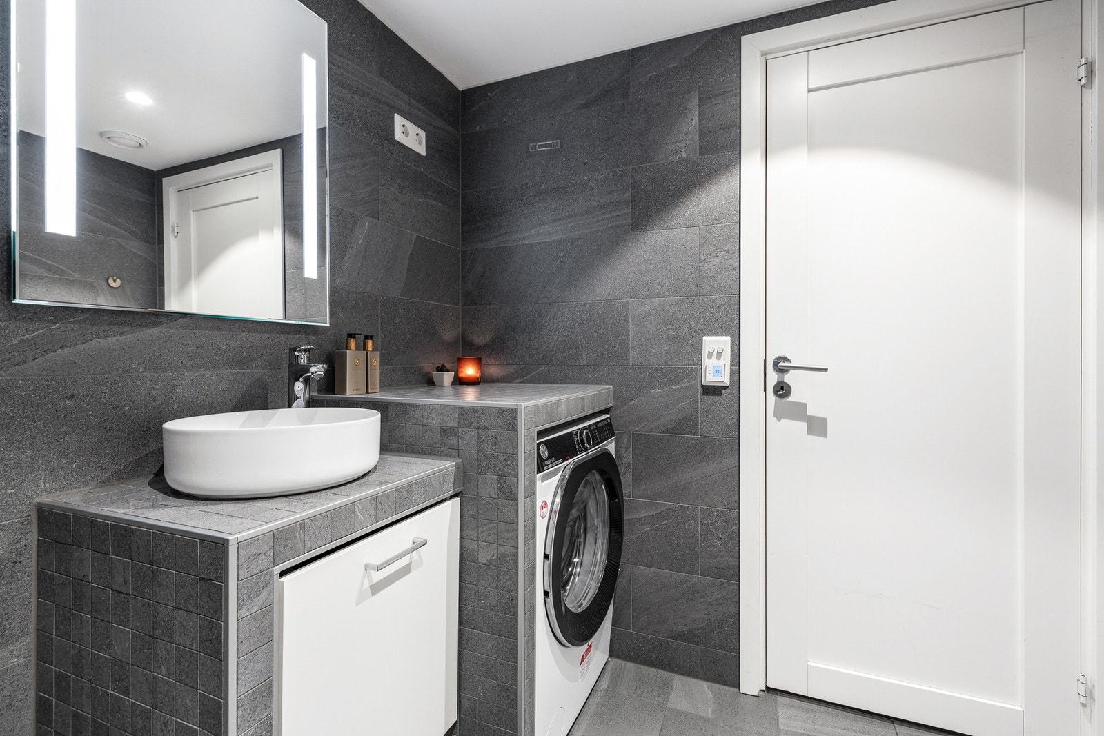 Videre er badet innredet med speil med integrert belysning og plassbygget innredning med flislagte benker og ovenpåliggende bolleservant Galleribilde