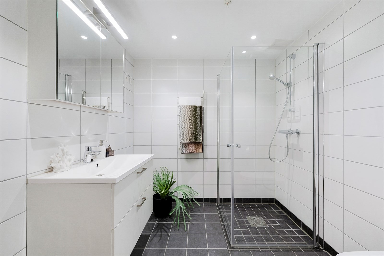 Moderne og tidløst bad med flislagte vegger og gulv med varme, ledspotter i tak, dusjhjørne med innfellbare dører i herdet glass og opplegg for vaskemaskin og tørketrommel Galleribilde