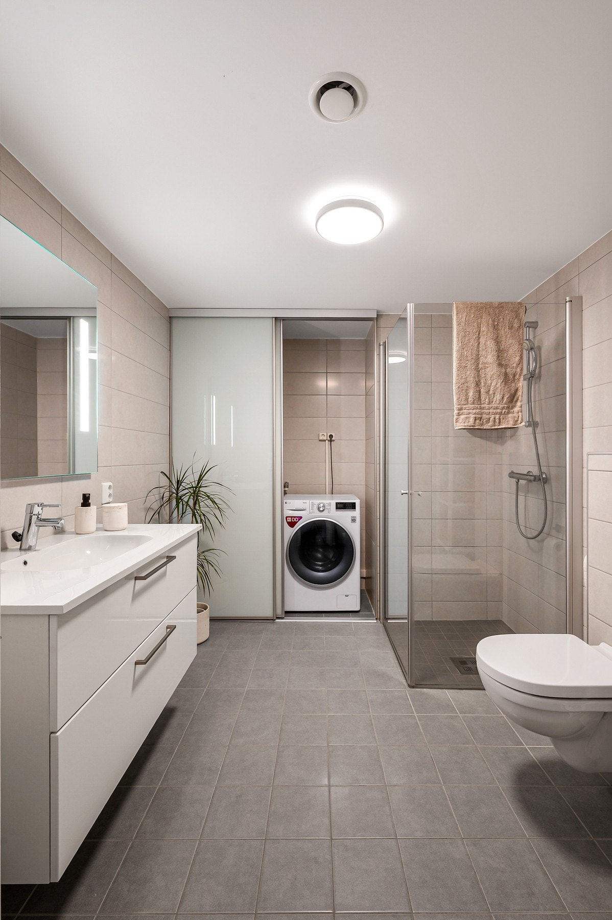 Badet har dusjhjørne med glassdører, vegghengt toalett og opplegg for vaskemaskin. Galleribilde