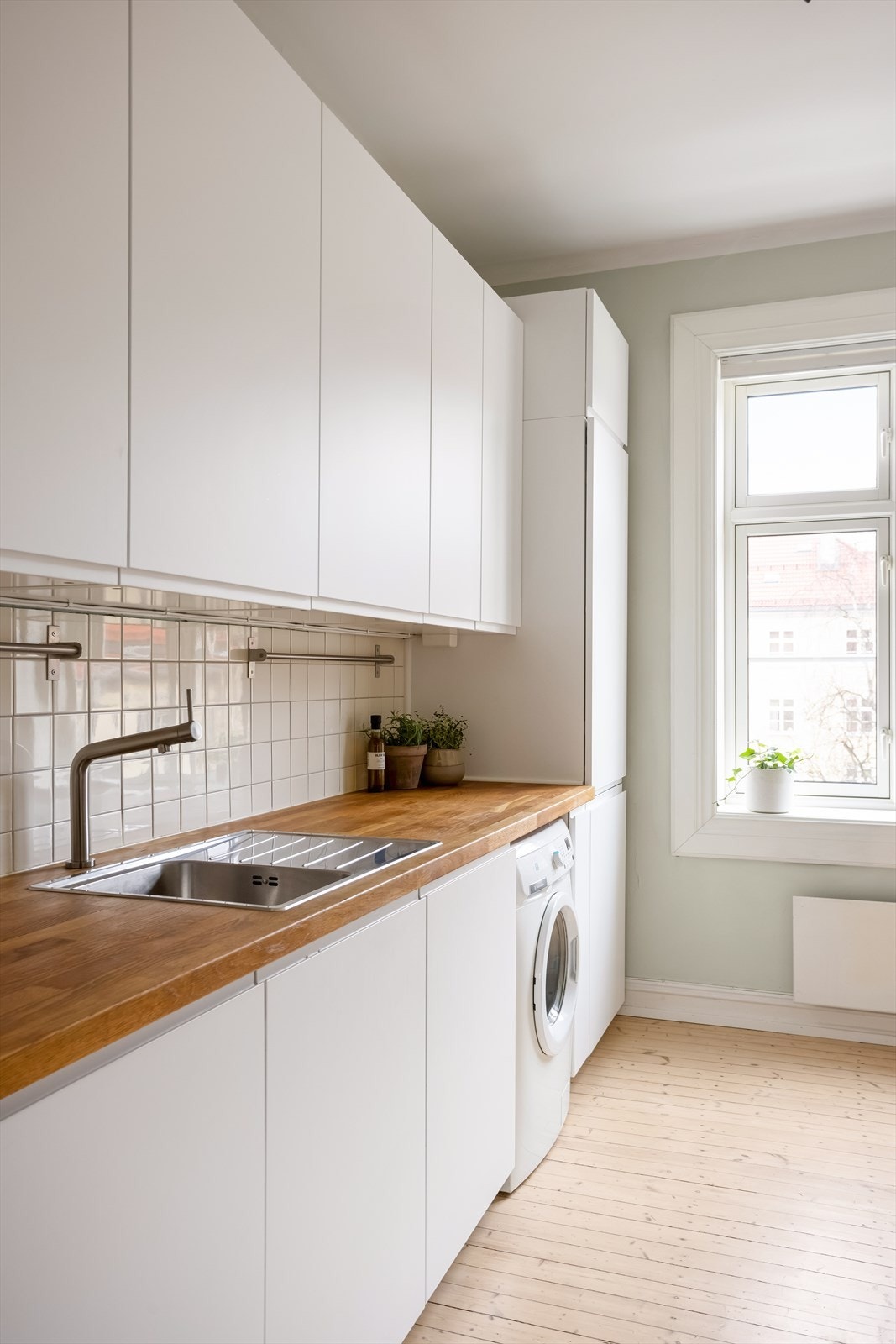 IKEA kjøkkeninnredning fra 2020 med glatte folierte fronter, benkeplate i tre med nedfelt kum i rustfritt stål, fliser på vegg over benk og ventilator med kullfilter. Galleribilde