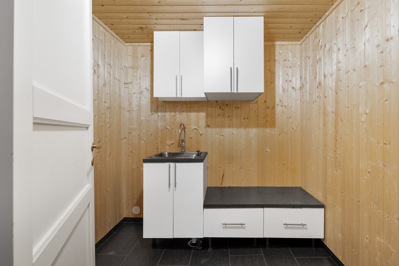 Praktisk vaskerom i underetasjen med panel på vegger og i himling, samt vinylbelegg på gulvet Galleribilde