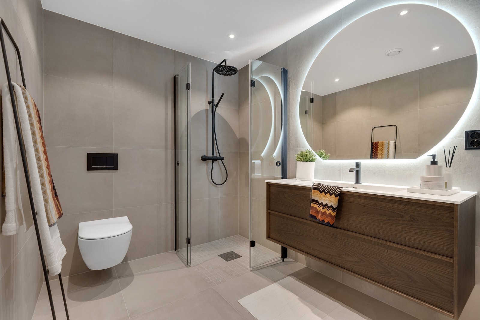 Hovedbadet. Stilrene og moderne material- og fargevalg, med blant annet helstøpt corian vask, stort rundt speil med integrert belysning, regndusj, 60x60 fliser på vegg og gulv og baderomsinnredning i mørk eik fra Korsbakken. Galleribilde