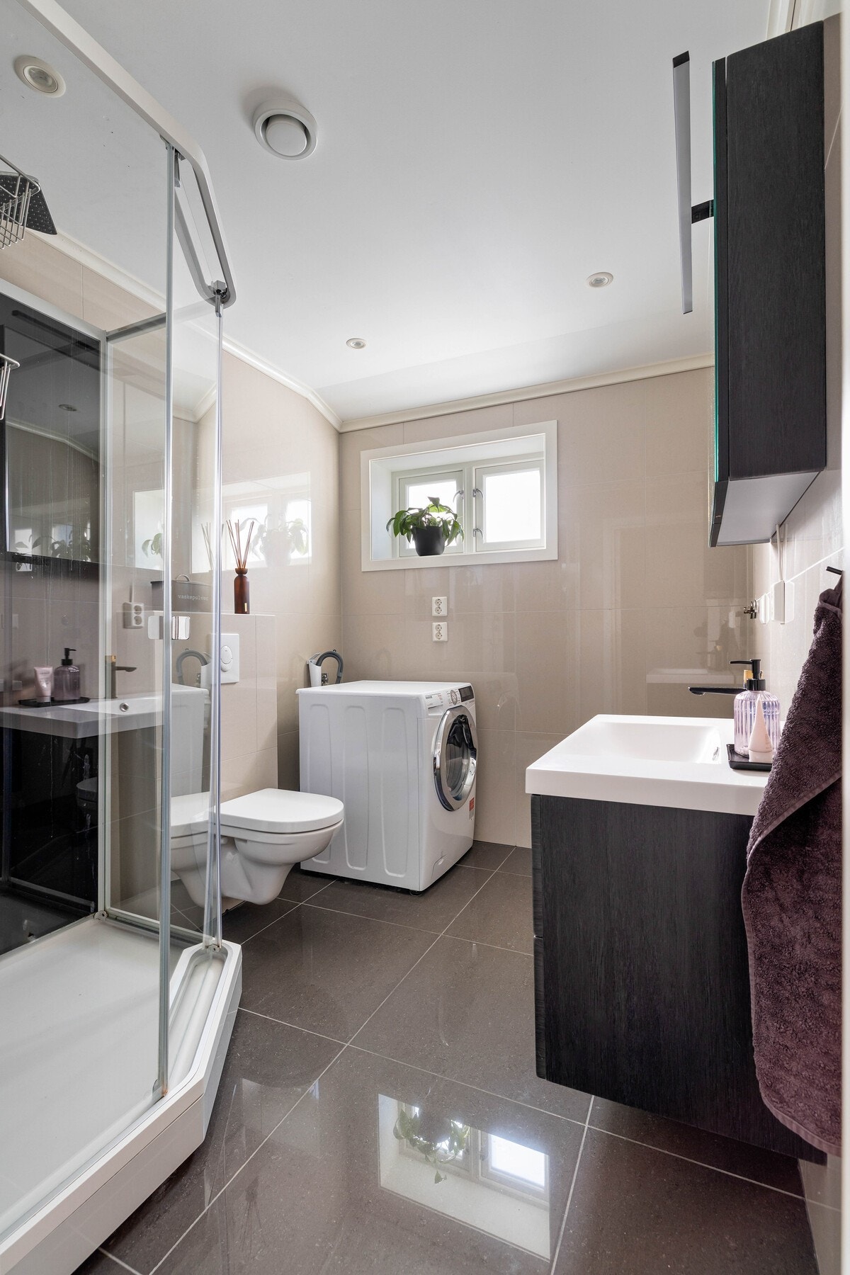 Moderne og pent bad med servant i stilren innredning, speilskap, dusjkabinett, vegghengt toalett og opplegg for vaskemaskin. Galleribilde