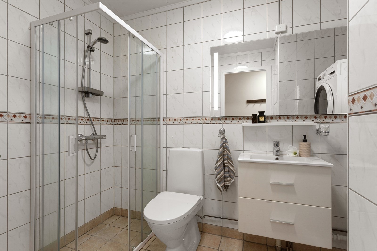 Badet er flislagt og har en praktisk utforming. Rommet er utstyrt med dusjhjørne med glassvegger, servantinnredning med oppbevaring og speil. Galleribilde