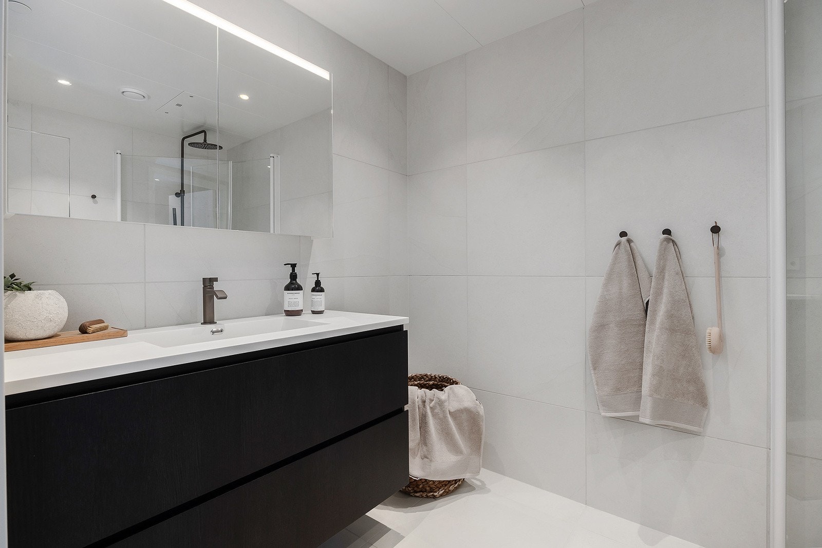 Badet er oppført med store 60x60 fliser, stor servant i mørkbeiset eikefinèr og downlights i himling. Speilskap med belysning. Galleribilde