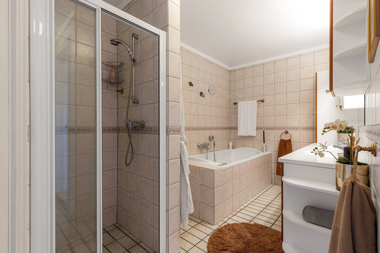 Vegghengt skap ved speil. Dusjhjørne med skyvedør av glass og metall. Vegghengt dusjarmatur. Flislagt boblebadekar. Vegghengt dusjarmatur. Galleribilde