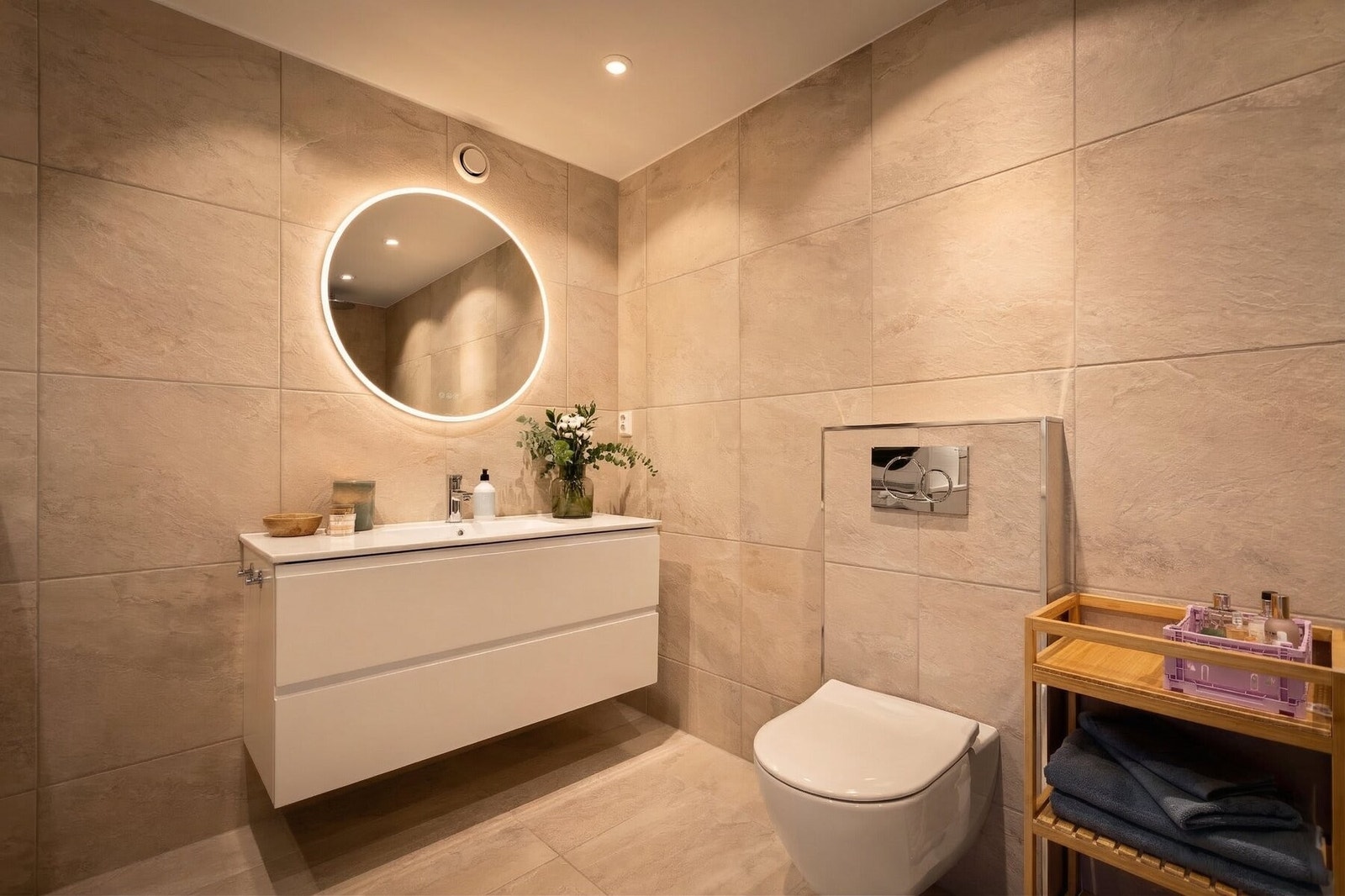 Badet er utstyrt med vegghengt toalett, servantmøbel med gode oppbevaringsmuligheter og speil med integrert belysning. Rommet har også en praktisk dusjnisje med dusjarmatur og opplegg for vaskemaskin og tørketrommel. Galleribilde