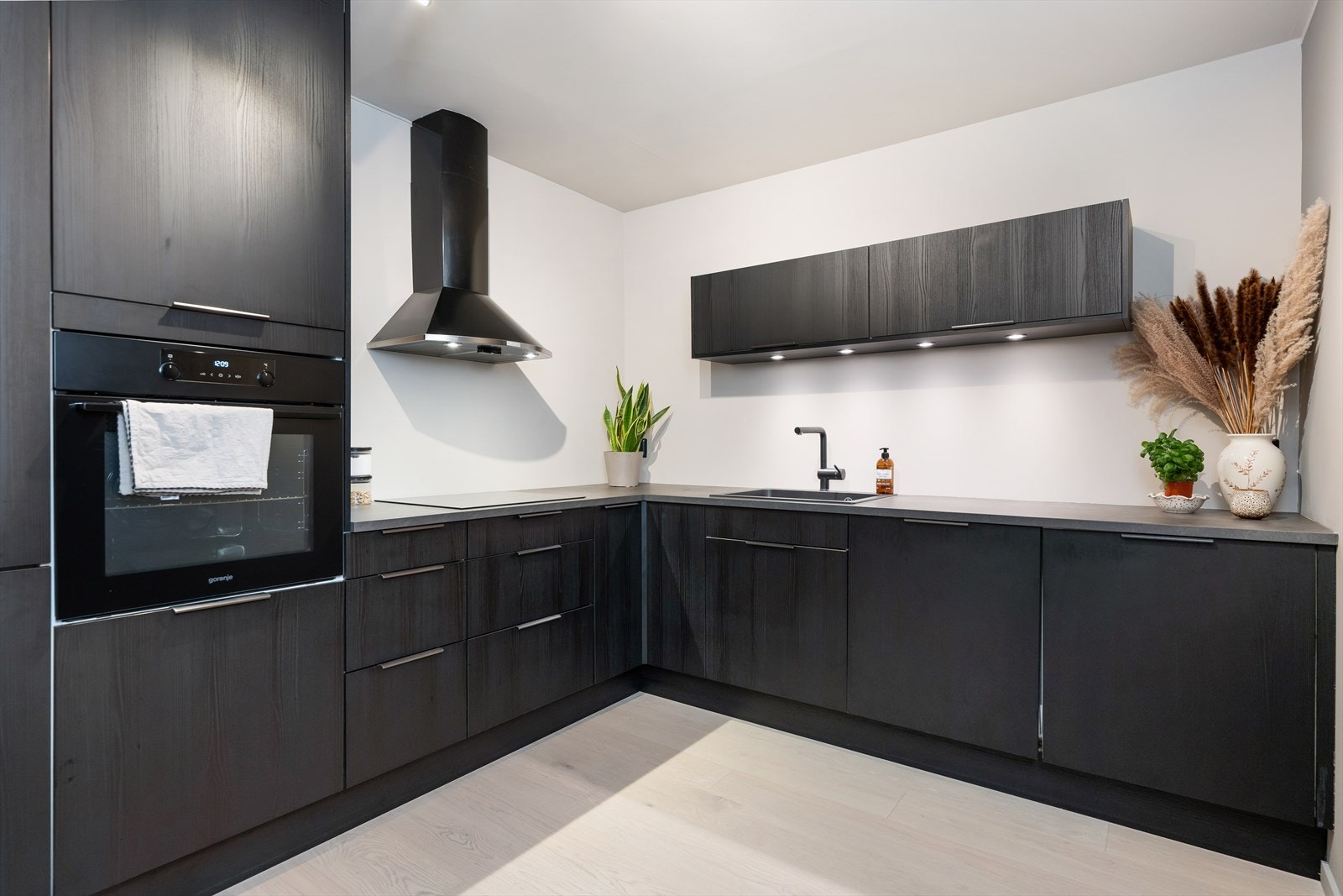 Stilrent kjøkken med slette, mørke fronter som gir et moderne uttrykk mot lyse vegger. Galleribilde