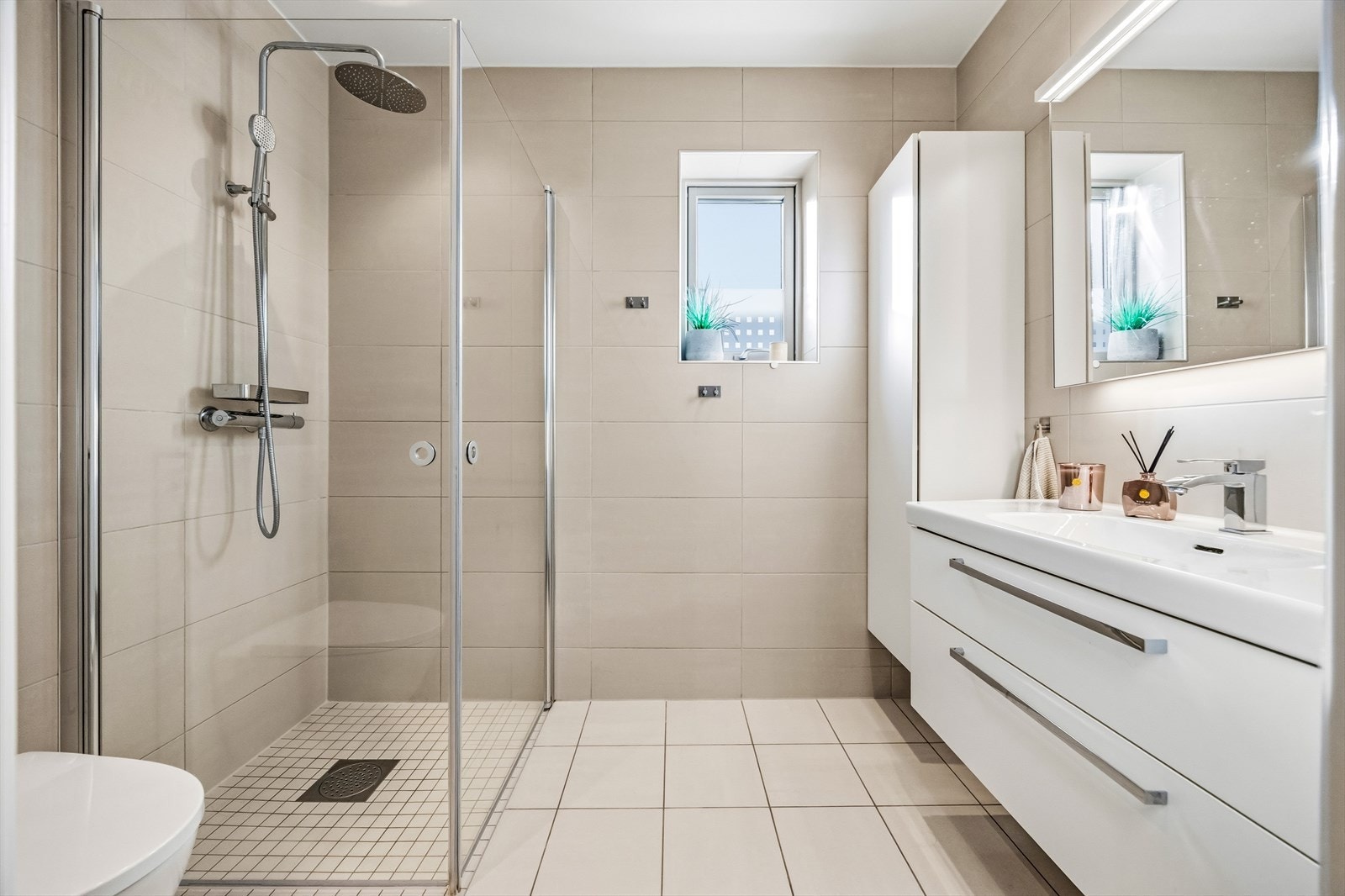 Lyst og hyggelig bad med regnfallsdusj, vegghengt wc og god lagringsplass for baderomsartikler. Galleribilde