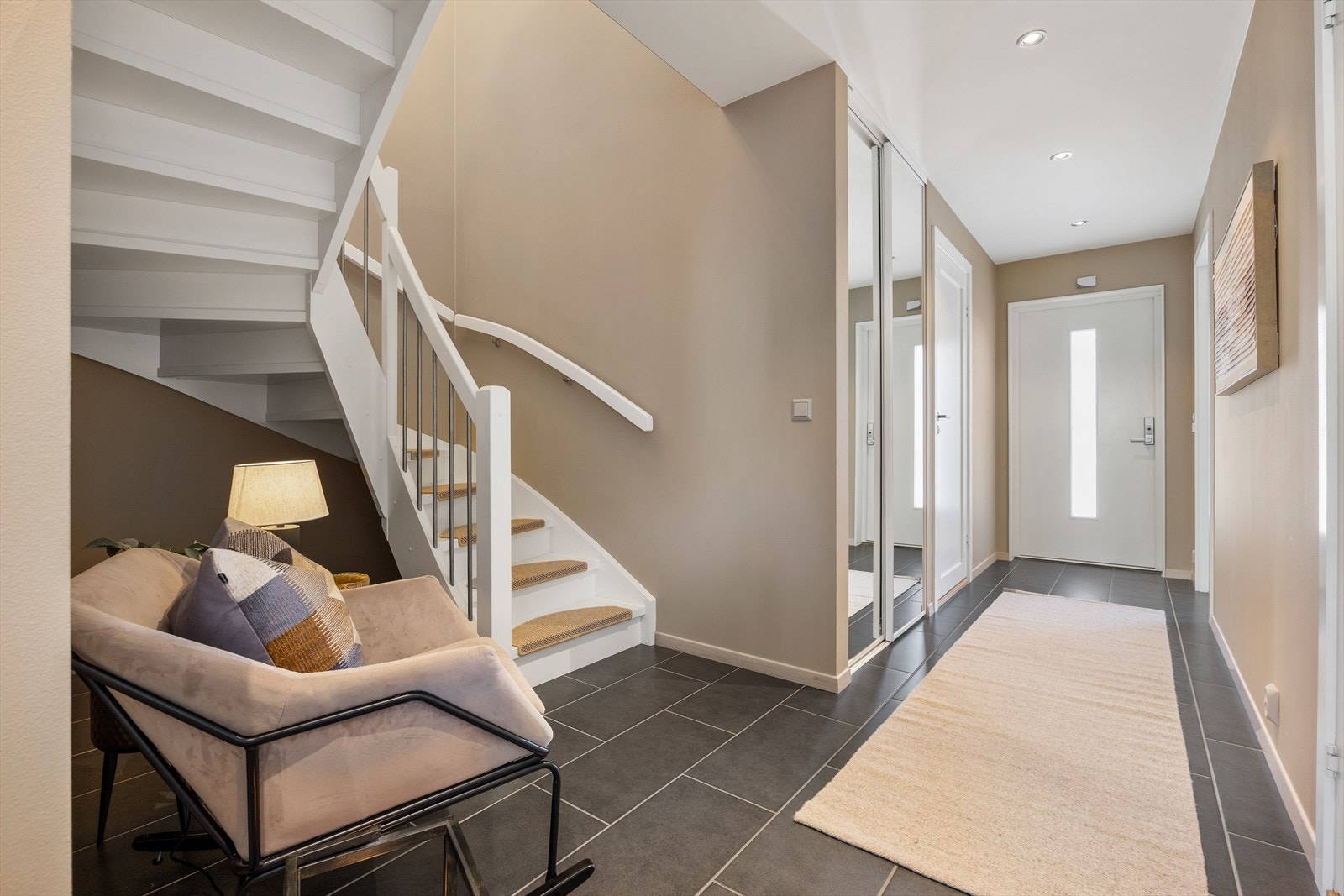 Gangen leder videre til etasjens øvrige rom og har en hvitmalt, lukket tretrapp med trappetrinnsteppe i trinnene som fører opp til 2. etasje. Galleribilde