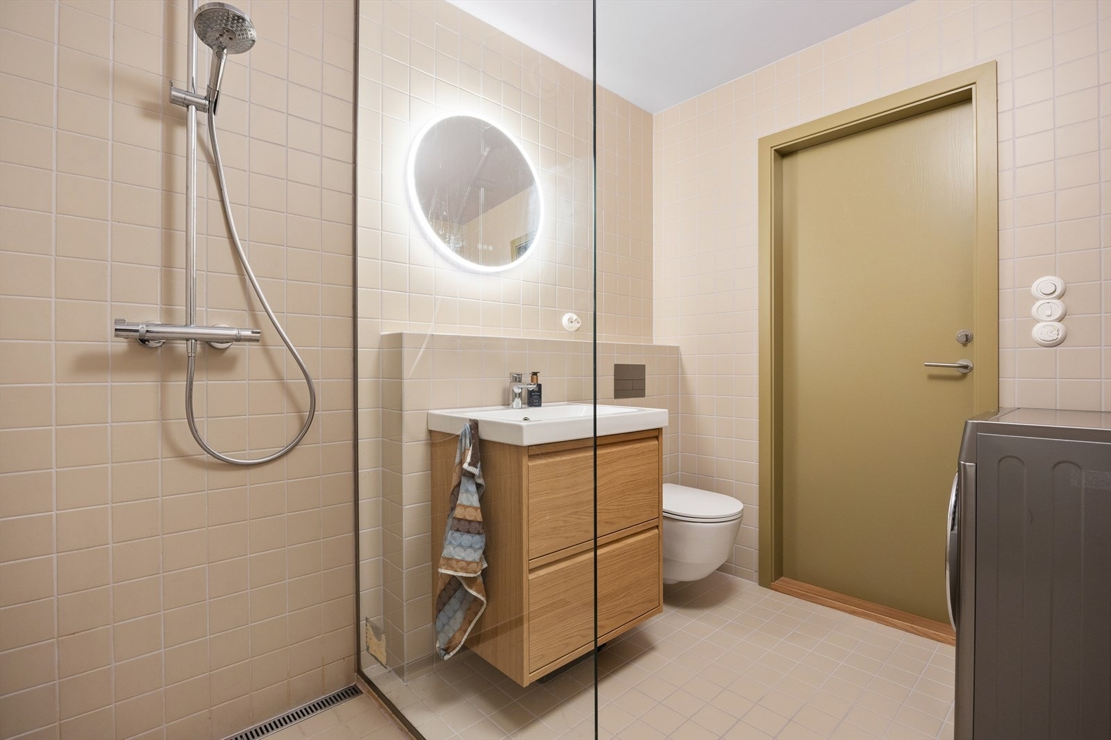 Et moderne bad (2024) av Murmester Myhre AS, har flislagte gulv med elektriske varmekabler, fliser på vegger og malt himling. Rommet er utstyrt med innredning med nedfelt servant, veggmontert toalett, dusjvegger/-hjørne og opplegg for vaskemaskin. Galleribilde