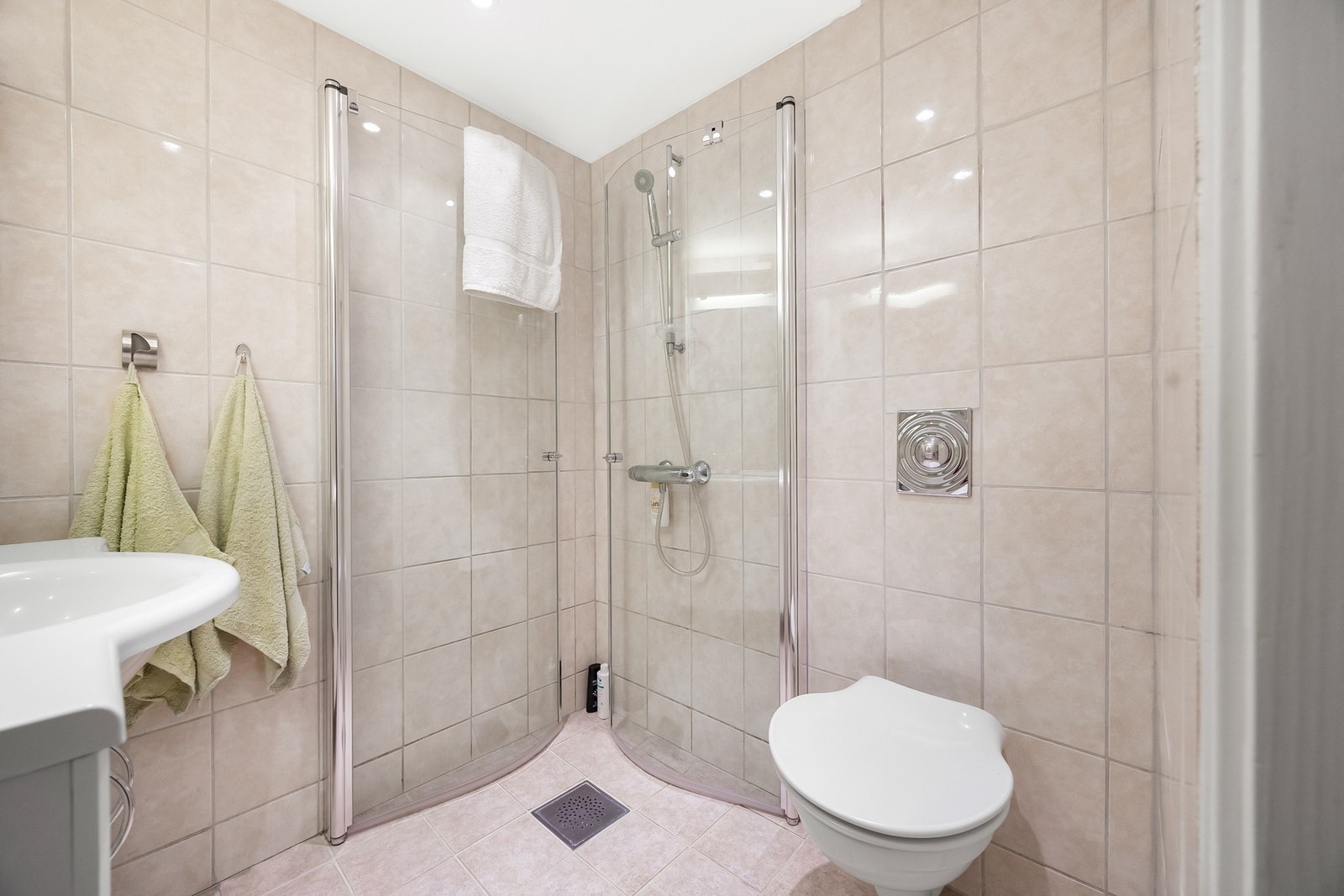 Badet er innredet med servantinnredning, speil på vegg over servant, vegghengt toalett og dusjhjørne med svingbare glassdører. Galleribilde
