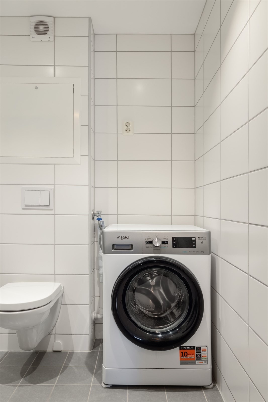 Praktisk nisje med plass og opplegg for vaskemaskin og tørketrommel over om ønskelig. Baderommet er også utstyrt med dusjhjørne med innfellbare glassdører og både hånd- og regnfallsdusj, samt vegghengt toalett. Galleribilde