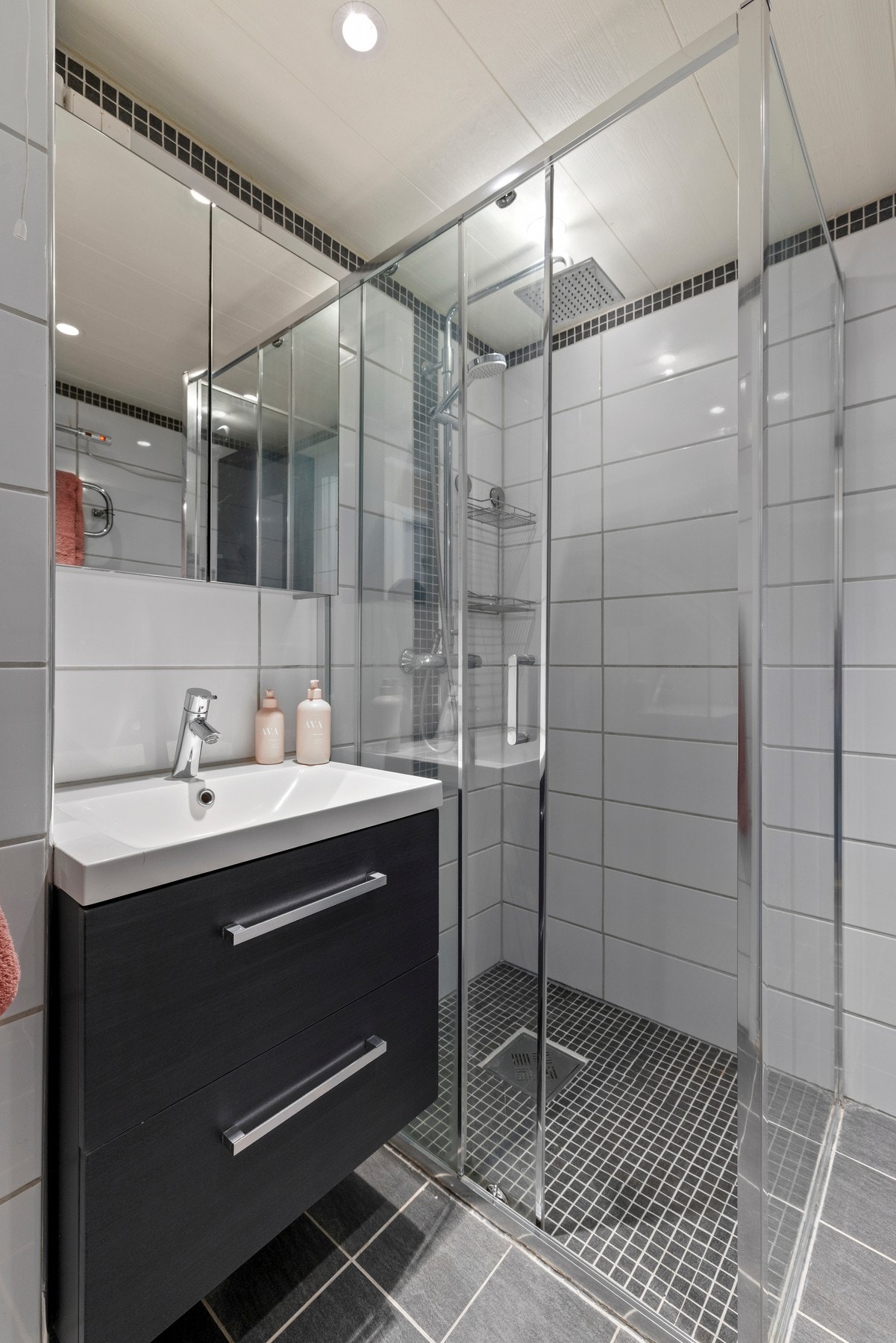 Badet har fliser på gulv og vegger, varmekabler i gulvet, servant med skap, speilskap og et dusjhjørne med regnfallsdusj Galleribilde