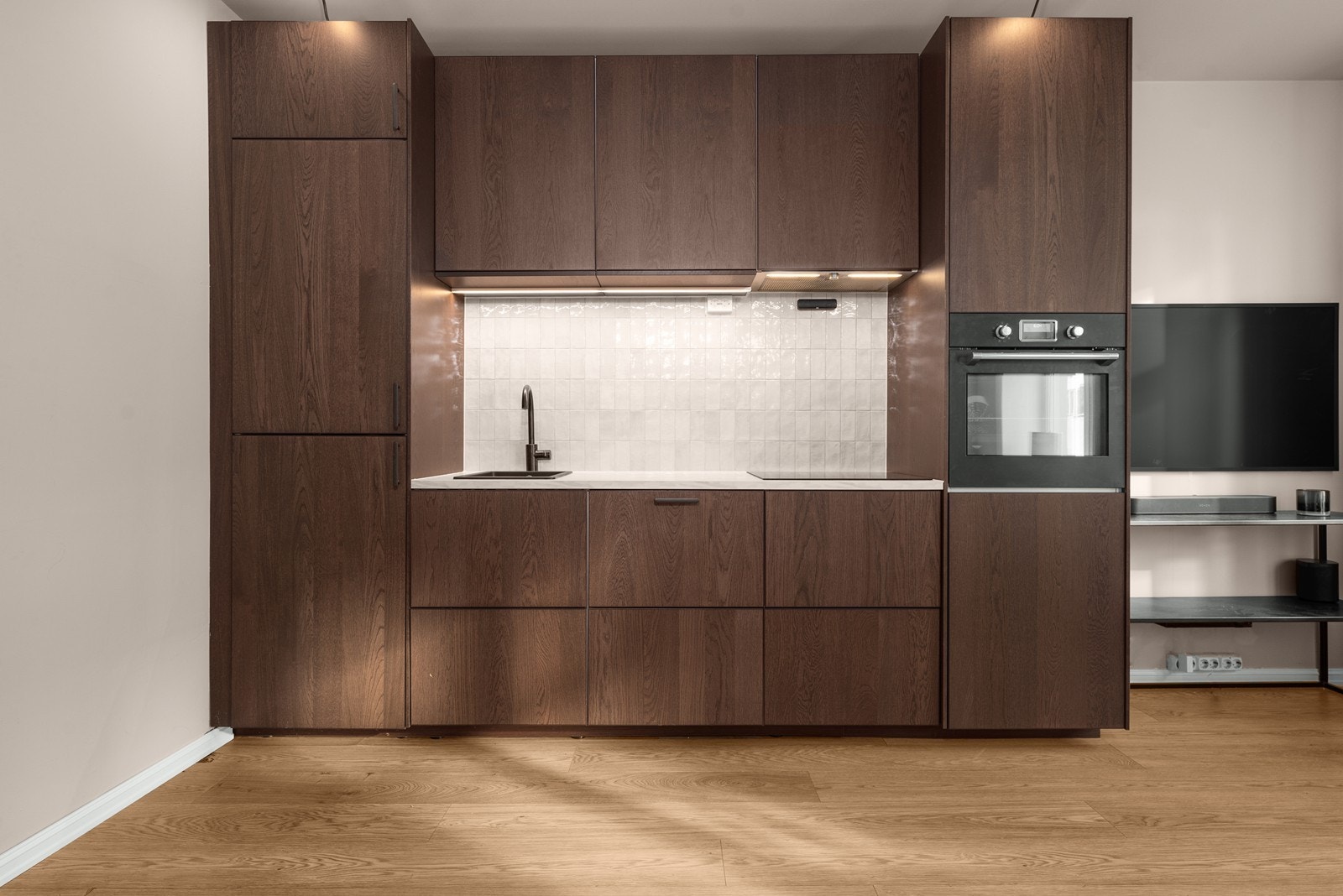 Stilrent og lekkert kjøkken med mørke fronter og integrerte hvitevarer som oppvaskmaskin og kjøl- og fryseskap. Galleribilde