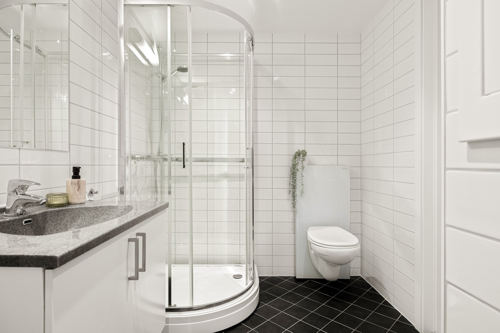 Badet er innredet med delikate overflater og inneholder vegghengt toalett, dusjkabinett, og baderomsinnredning. Galleribilde