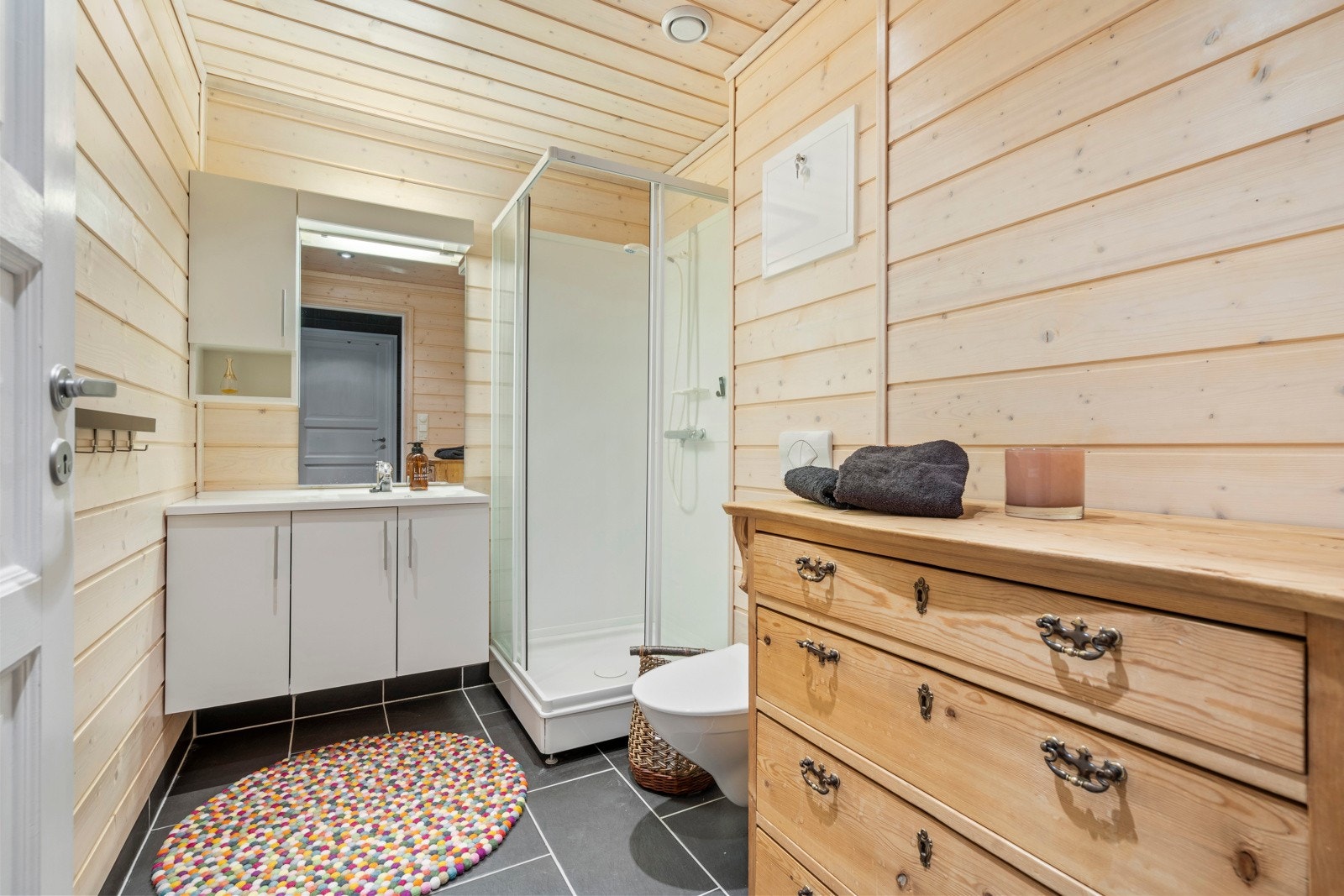 Badet har fliser med varme i gulvet og panelte vegger som gir en lun hyttefølelse. Her finner du servant med moderne hvit innredning, vegghengt toalett og dusjkabinett. Galleribilde