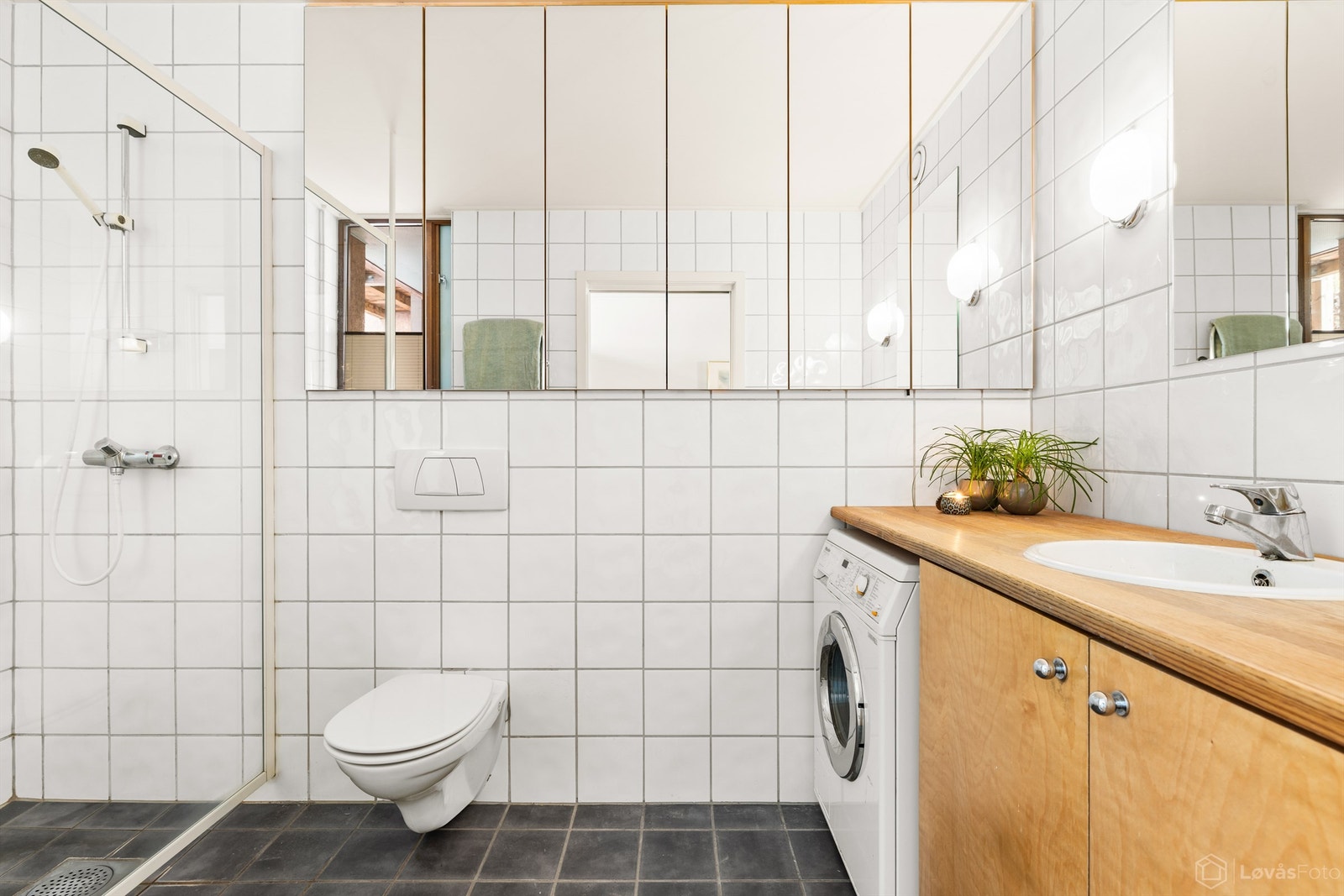 Badet er flislagt og utstyrt med vegghengt toalett, dusjhjørne og opplegg for vaskemaskin. Galleribilde