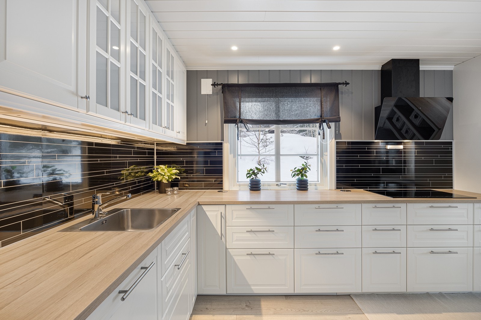 Innredningen har hvite, profilerte fronter, vitrinedører, takhøye skap og lys laminatbenkeplate med nedfelt kum i stål. Veggene over benken er kledd med sorte plater i flisimitasjon som står godt til resten av interiøret. Galleribilde