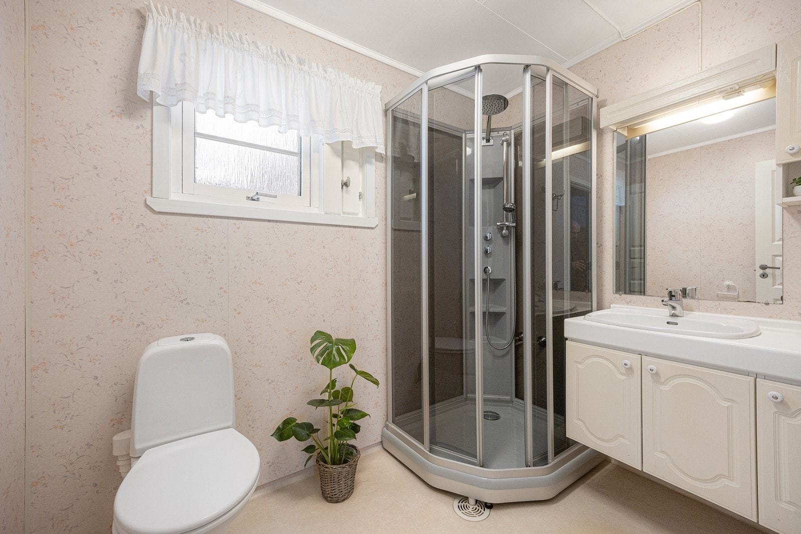 Baderomsinnredningen har lys, profilerte fronter og består av en nedfelt servant på en skapseksjon, et veggskap og et speil med belysning. Videre har badet et dusjkabinett fra 2014 og et gulvmontert toalett. Galleribilde