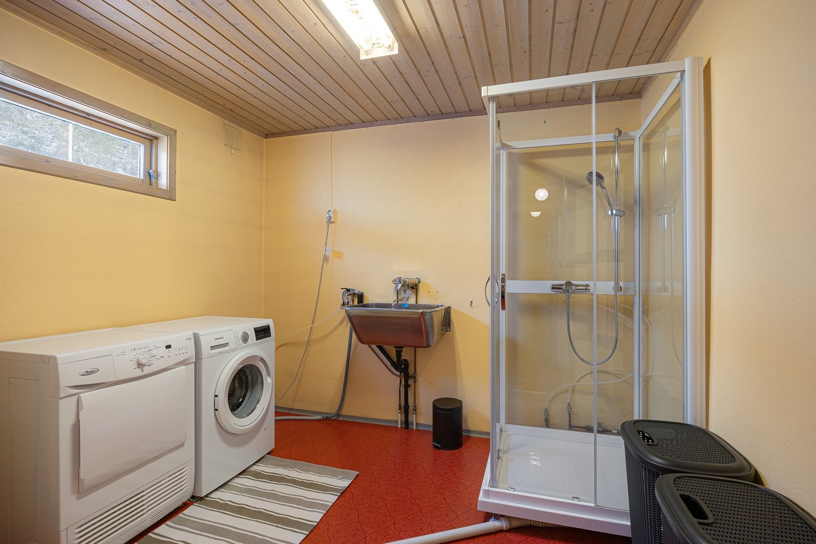 Vaskerommet ligger i underetasjen og har gulmalte murvegger og rødt belegg på gulvet. I tillegg til skyllekum og opplegg for vaskemaskin er rommet utstyrt med et dusjkabinett fra 2014. Galleribilde