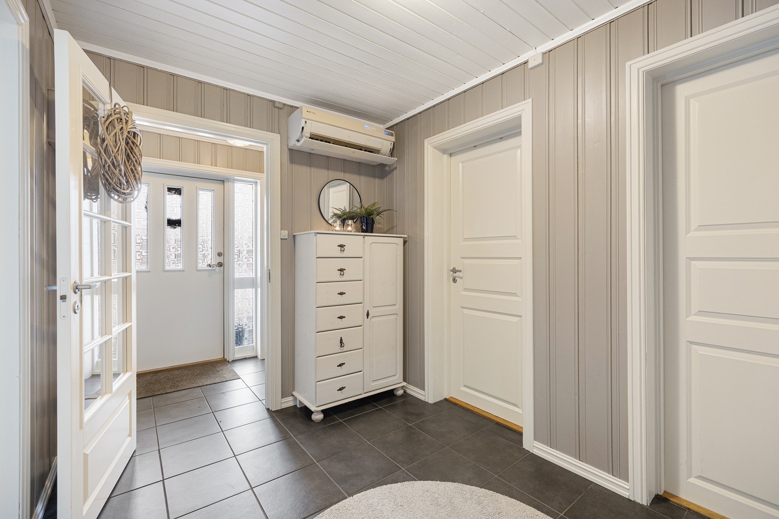 Yttertøyet ryddes enkelt bort i et hvitt, dobbelt garderobeskap i entreen. Farge- og materialkombinasjonen fortsetter inn i hallen hvor det også er montert en luft-til-luft varmepumpe. Galleribilde