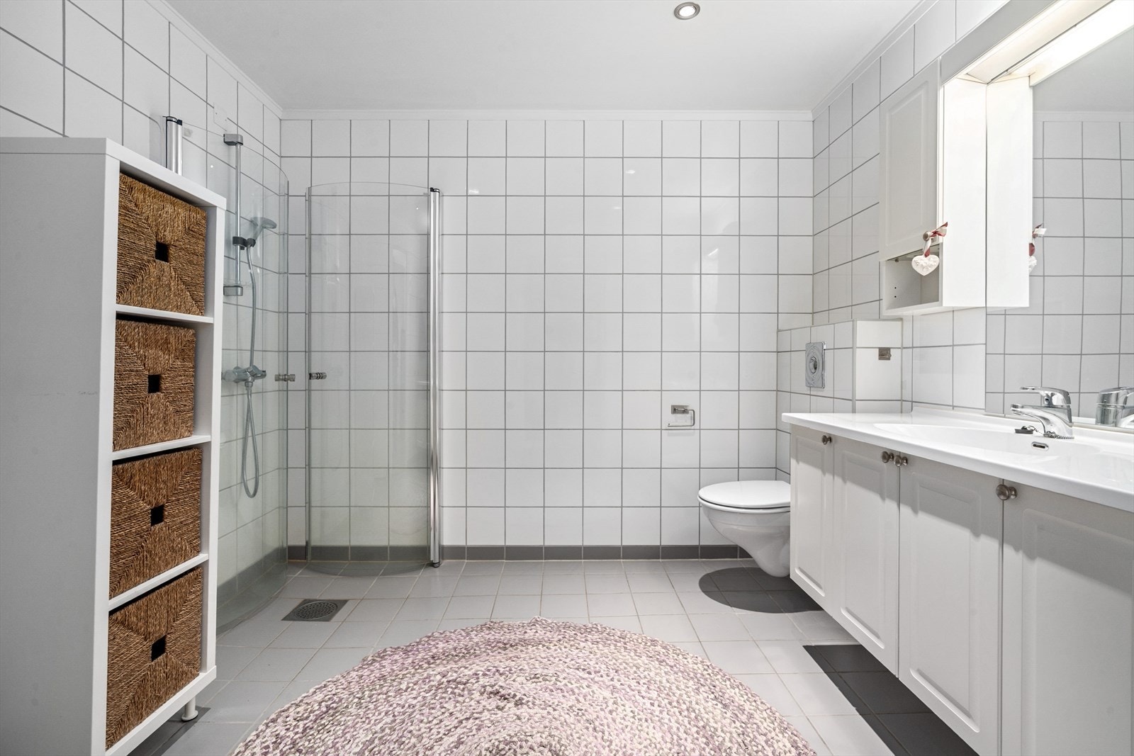 Stilrent, flislagt bad med elektrisk gulvvarme for god komfort. Rommet er utstyrt med vegghengt toalett, dusjgarnityr med buede dusjdører og røropplegg for vaskemaskin. Galleribilde