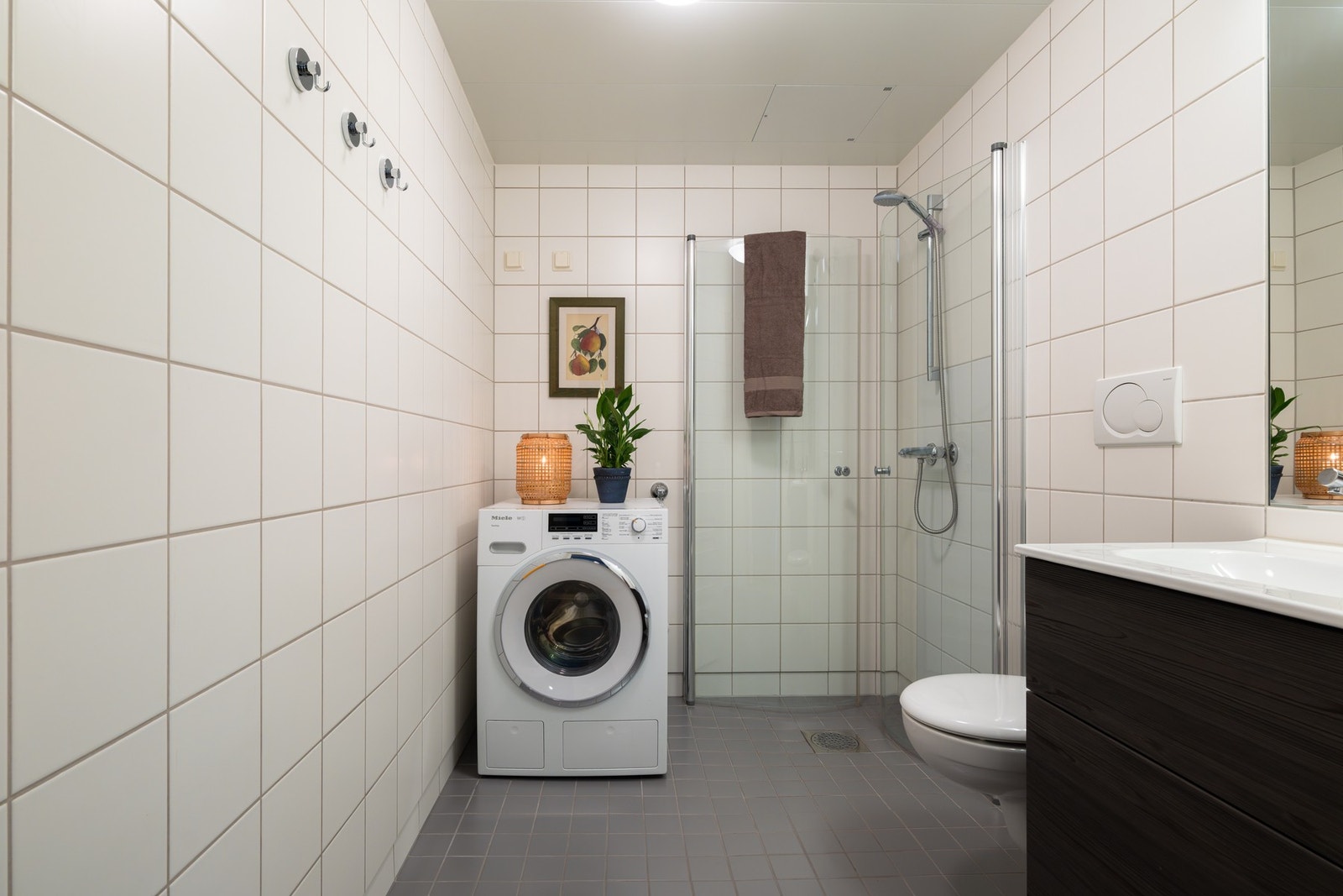 Badet er innredet med dusjhjørne med svingbare glassdører som frigjør plass på gulvet og vegghengt toalett. Galleribilde