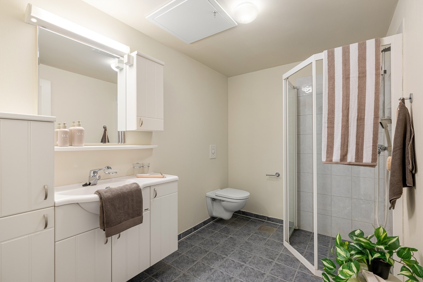 Badet er innredet med vegghengt baderomsmøbel med vask, vegghengt toalett, et dusjhjørne med glassvegger og opplegg for vaskemaskin. Galleribilde