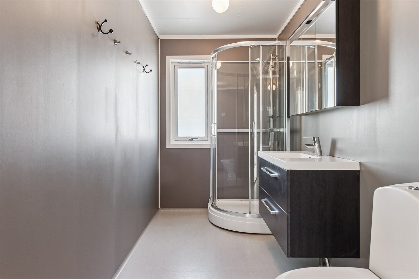 Badet i første etasje er utstyrt med dusjkabinett, toalett og servant med oppbevaring. Rommet har veggplater fra byggeåret som er malt i nyere tid. Galleribilde