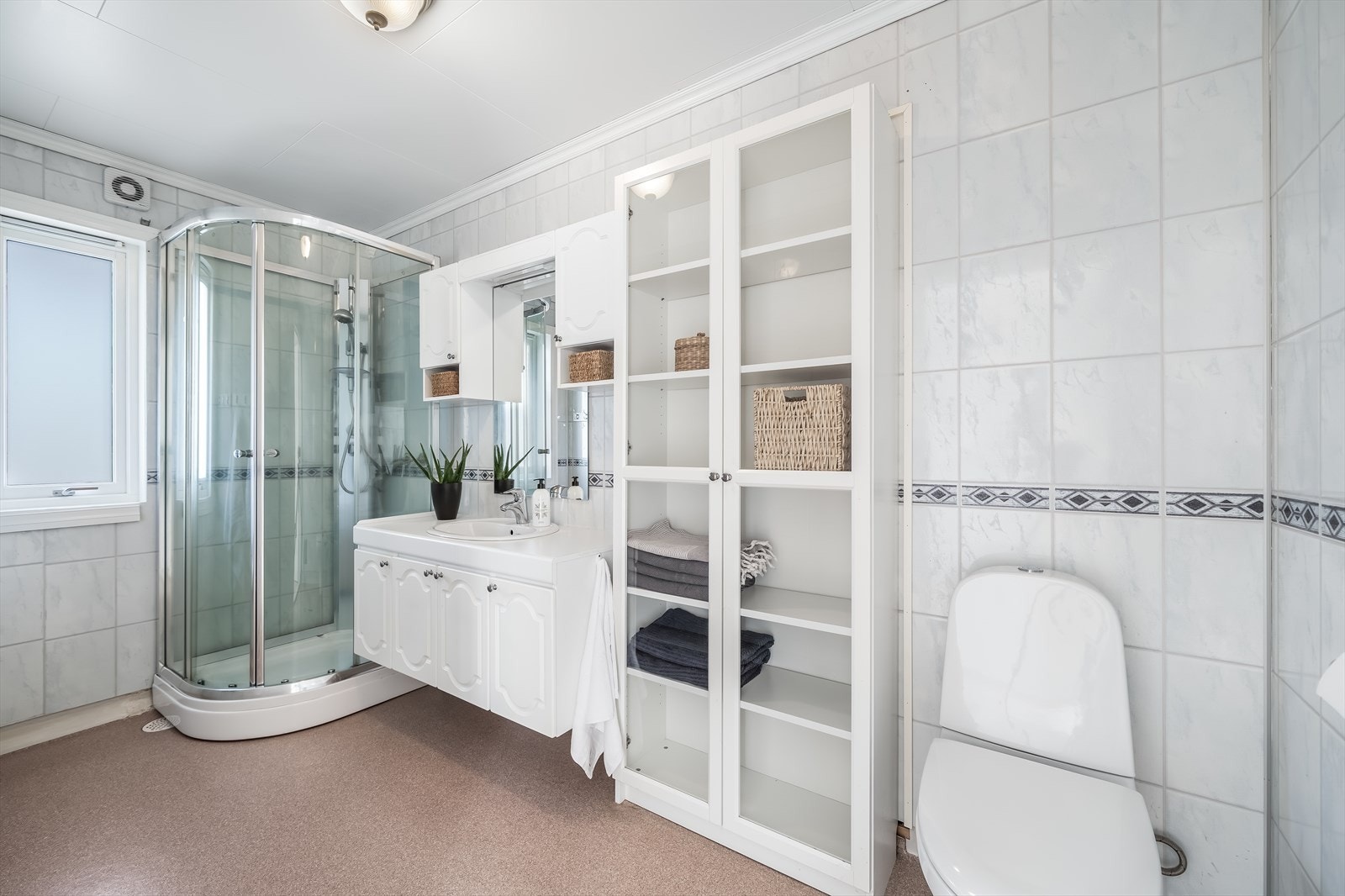 Bad med belegg på gulv og baderomsplater på vegg. Innredet med baderomsinnredning, toalett og dusjkabinett. Tidligere gikk det dør inn til soverommet (nå tv-stue) bak vitrineskapene. Galleribilde