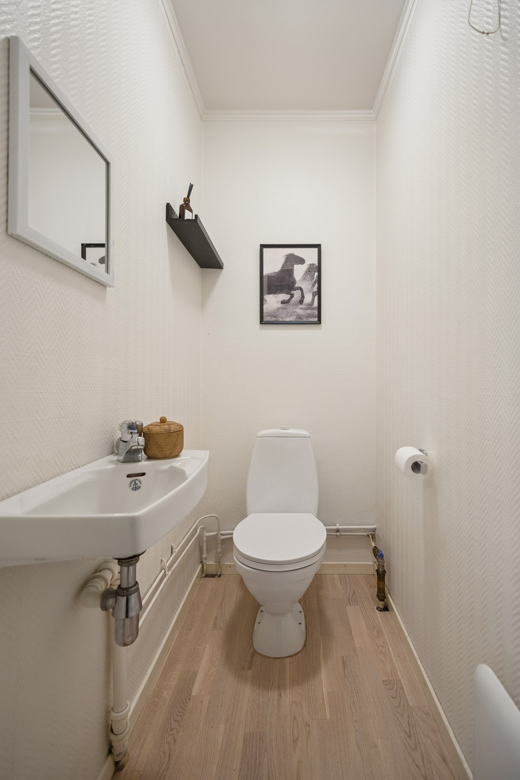 Praktisk toalettrom med parkettgulv, malte vegger, gulvmontert toalett og vegghengt servant. Galleribilde