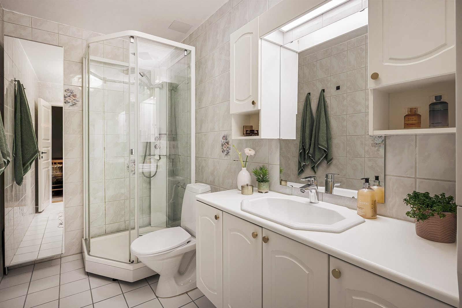 Badet er helfliset med lyse fliser og praktisk innredet med baderomsmøbel, speil med skap rundt, vegghengt toalett og dusjkabinett. Galleribilde