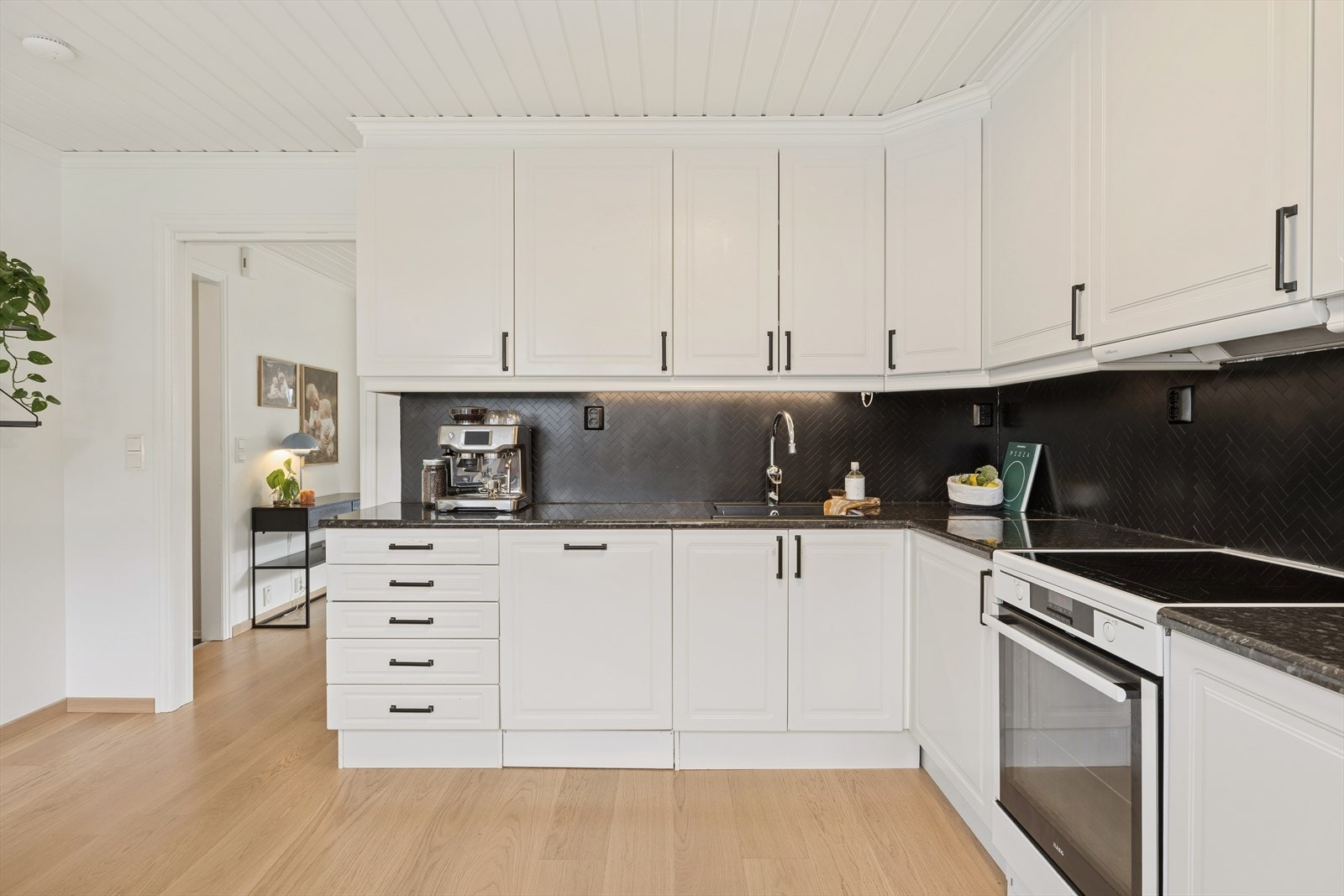 Kjøkkenet har en tidløs innredning fra Sigdal med hvite, profilerte fronter og laminert benkeplate med planlimt sort kum. Galleribilde