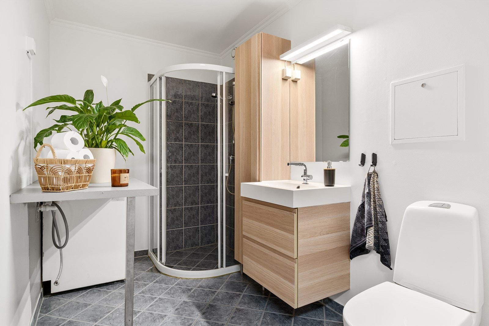 Bad/vaskerom med fliser på gulv med varmekabler under. Dusjhjørne, vask i seksjon , vegghengt skap med oppbevaringsplass og speil med belysning. WC. Galleribilde