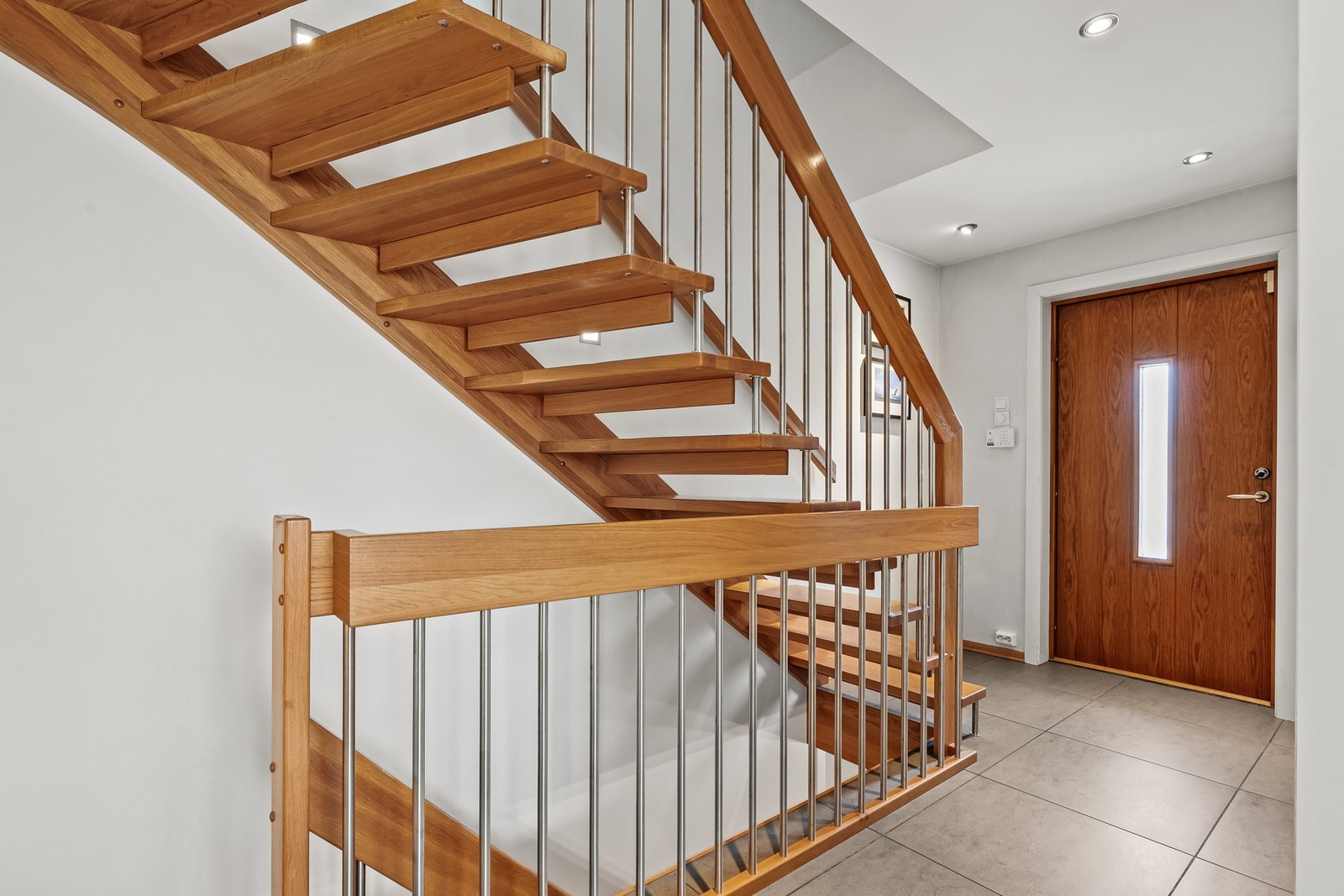 Vel inne blir man ønsket velkommen i en luftig entré med lysmalte vegger, downlights i himlingen og grå fliser på gulv med gulvvarme. Flott trapp fra 2012. Galleribilde